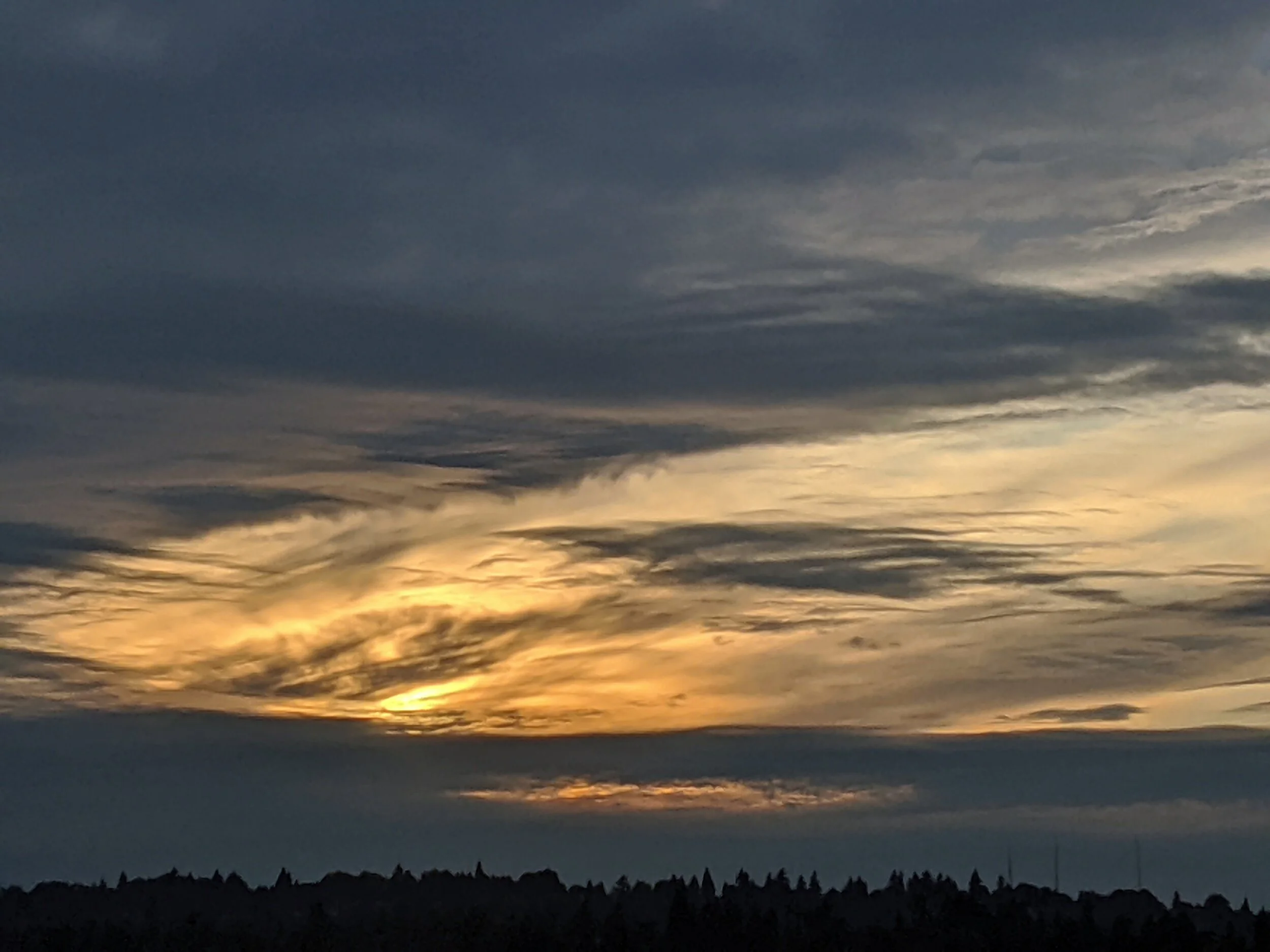  The setting sun illuminates wispy clouds in between the dark horizon and dark clouds at the top of the image 