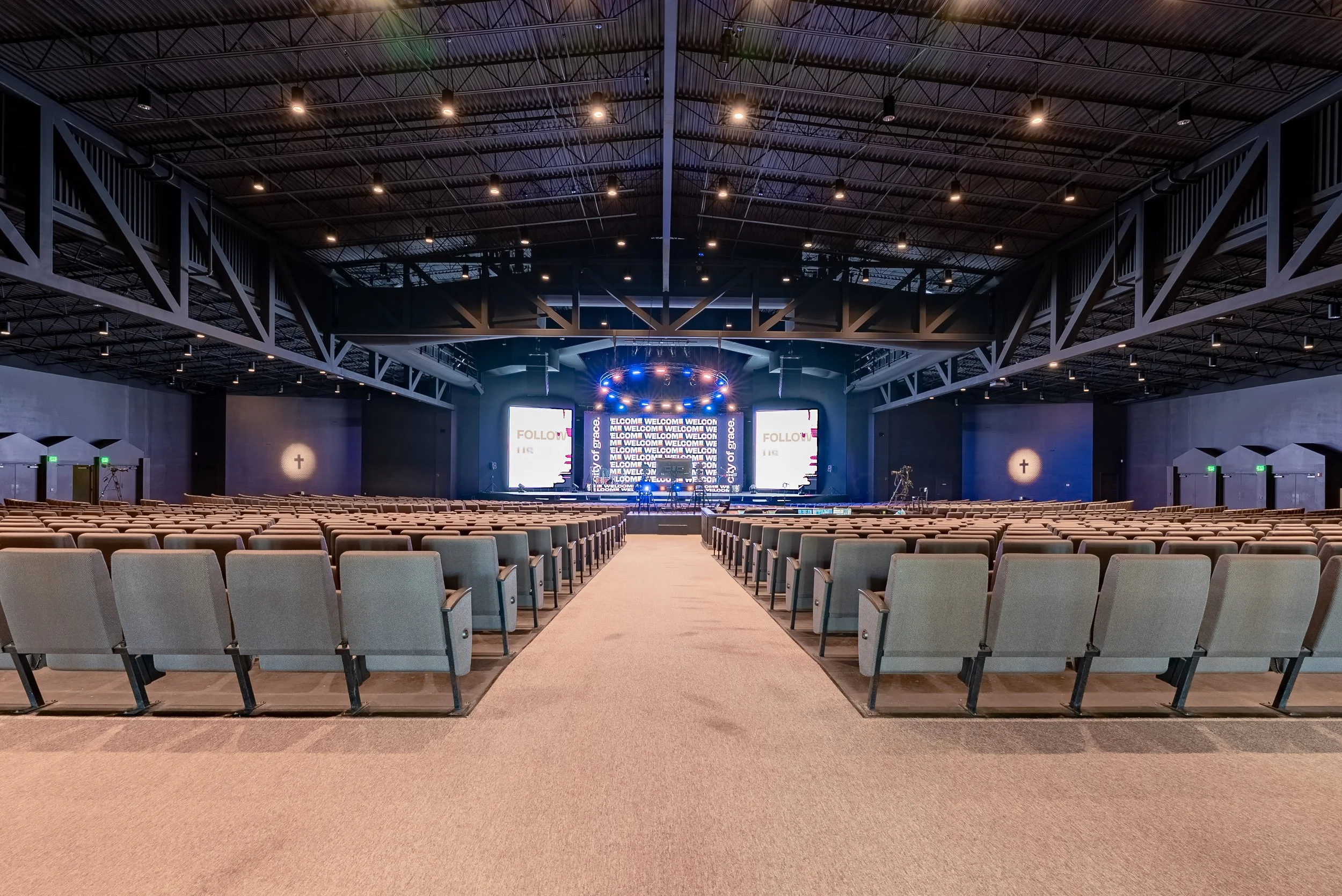Empty auditorium or conference hall with rows of chairs facing a stage with large LED screens and lighting equipment.
