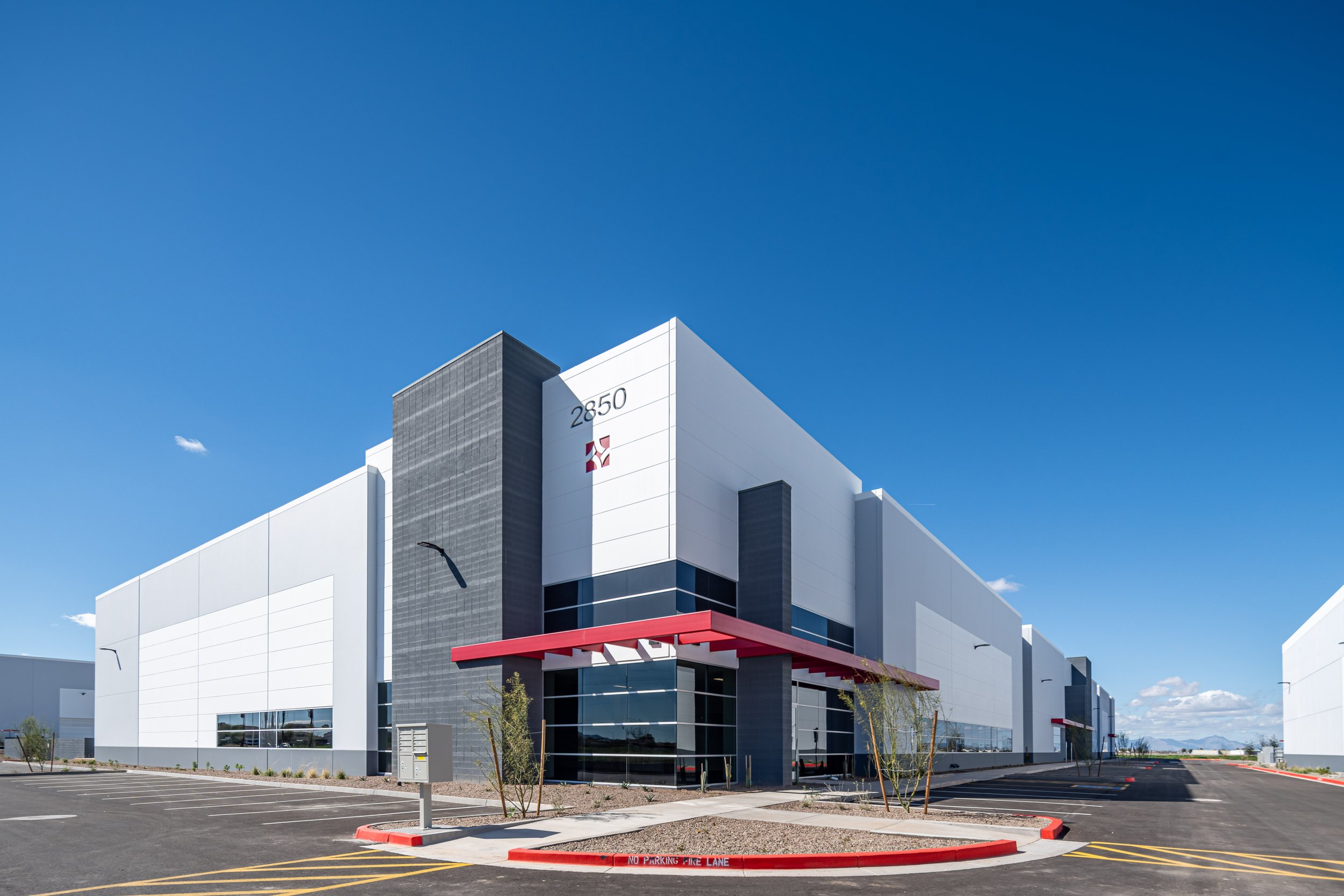 Modern industrial building with a white exterior, red canopy, and parking lot under a clear blue sky.