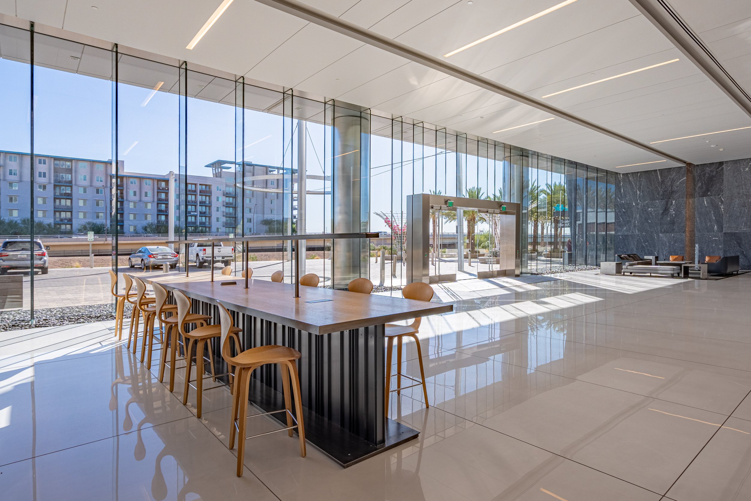 Modern hotel lobby with large glass windows, sitting area with chairs, and high ceiling.