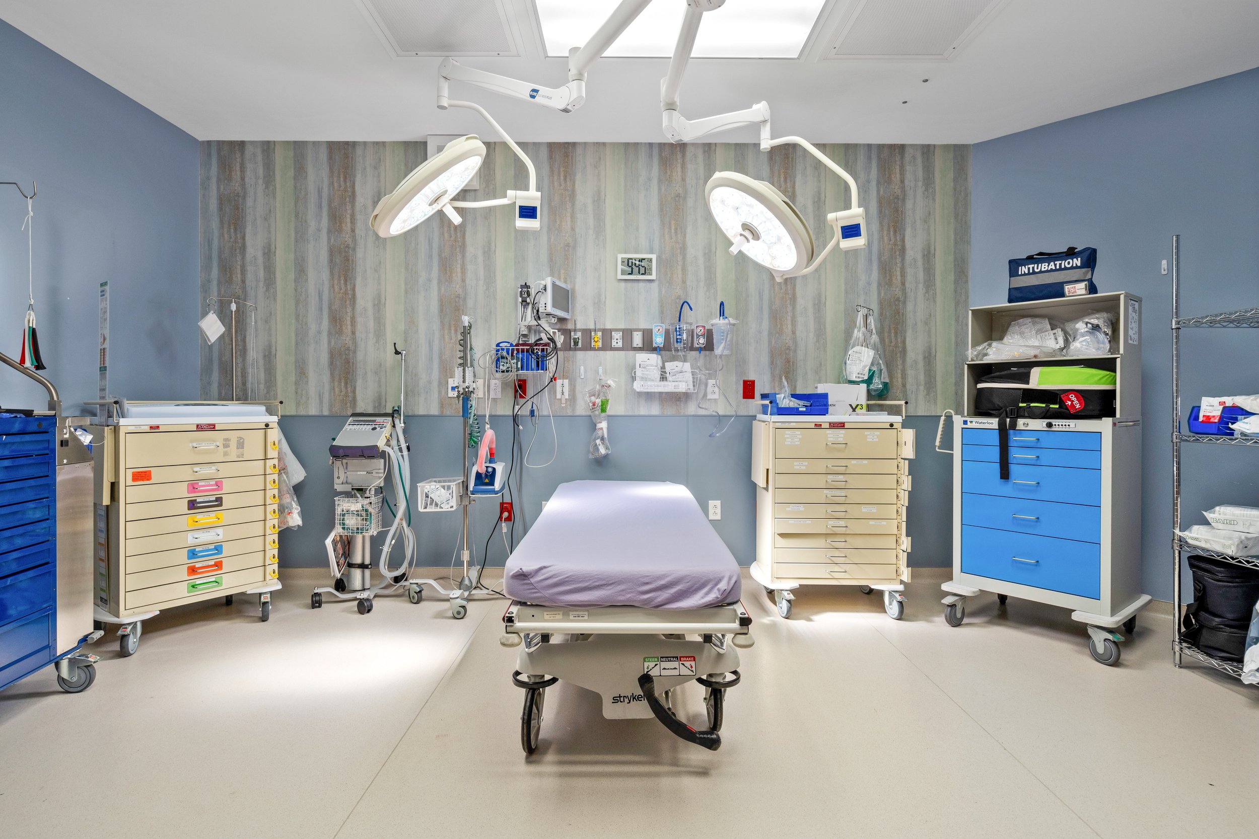 An empty hospital operating room with medical equipment, surgical lights, and a hospital bed in the center.
