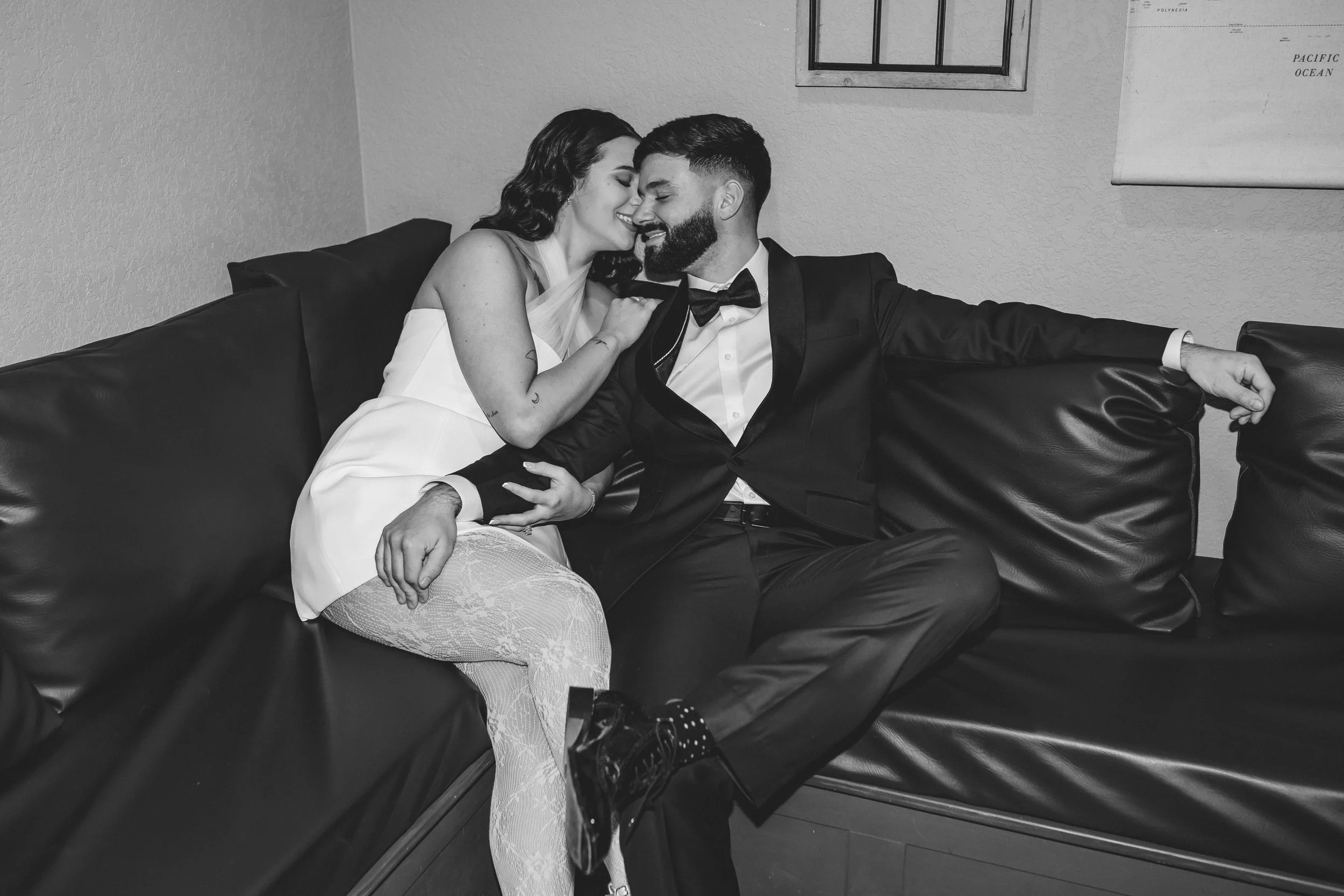 Romantic documentary wedding portrait of bride and groom sitting on a black leather couch