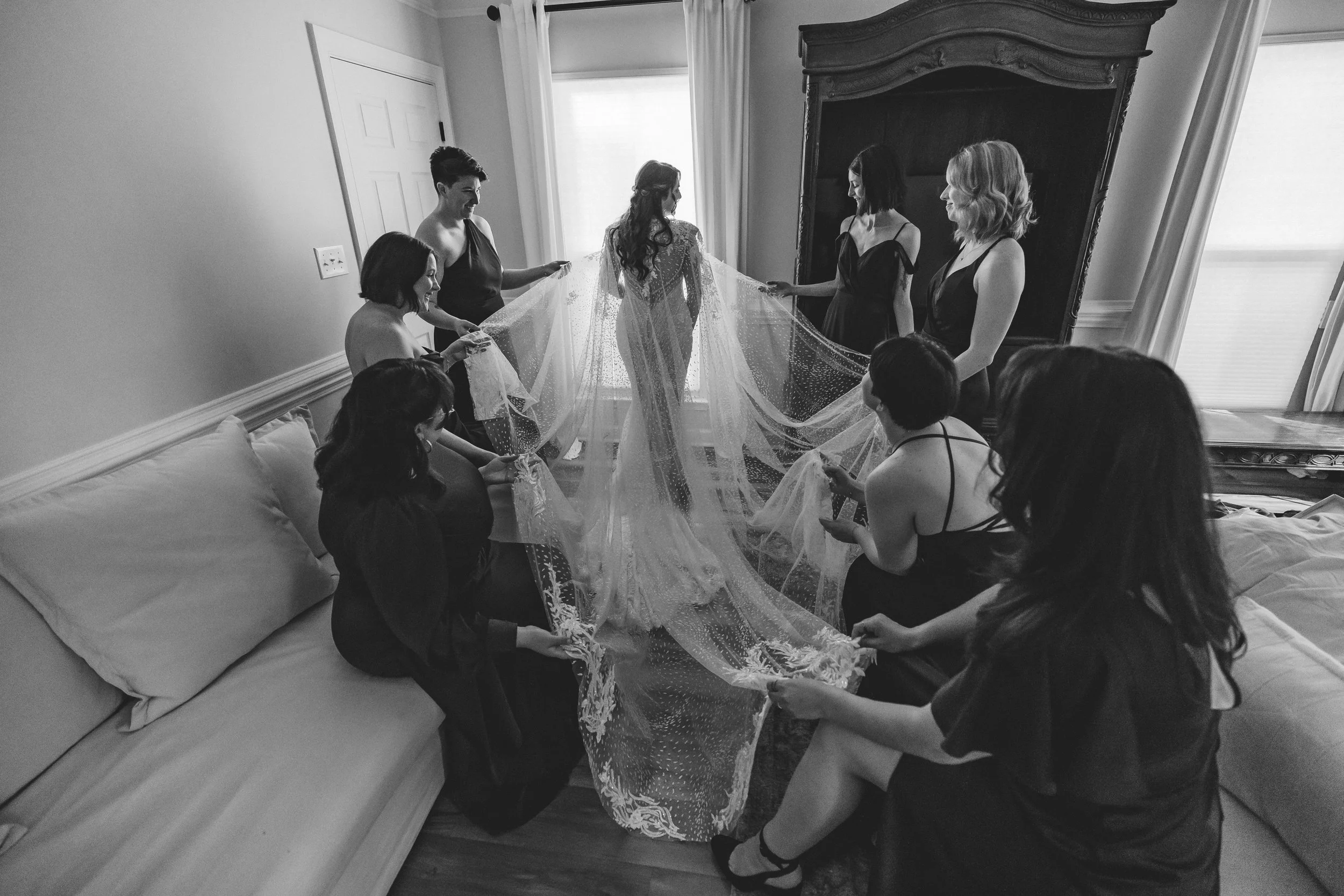 Charlotte, NC bride in a wedding dress standing in the center of a room, surrounded by her bridesmaids who are helping her with her dress and veil.