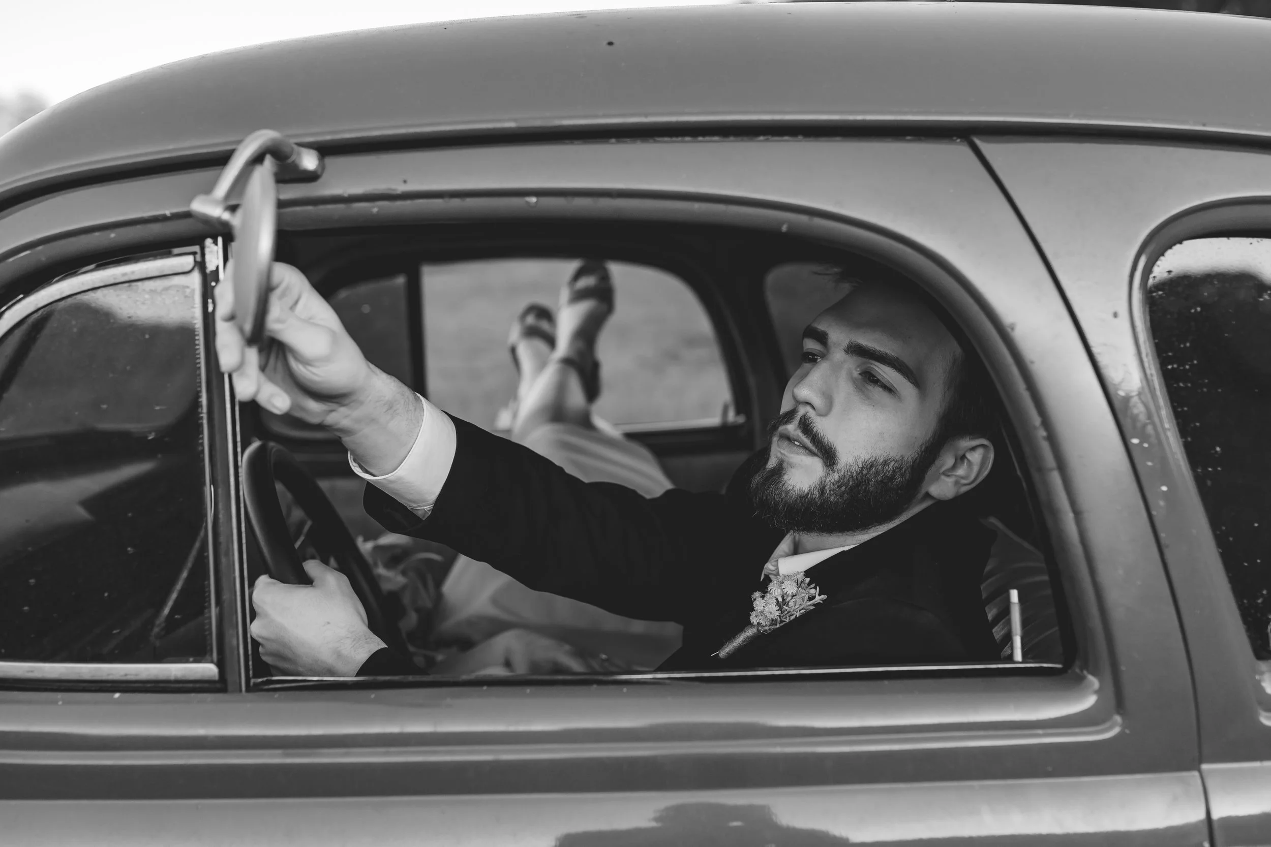 Peachtree City weddings, couple sitting in the driver's seat of a vintage car, looking out the window, with her legs up on the back seat, wearing a dress and heels.