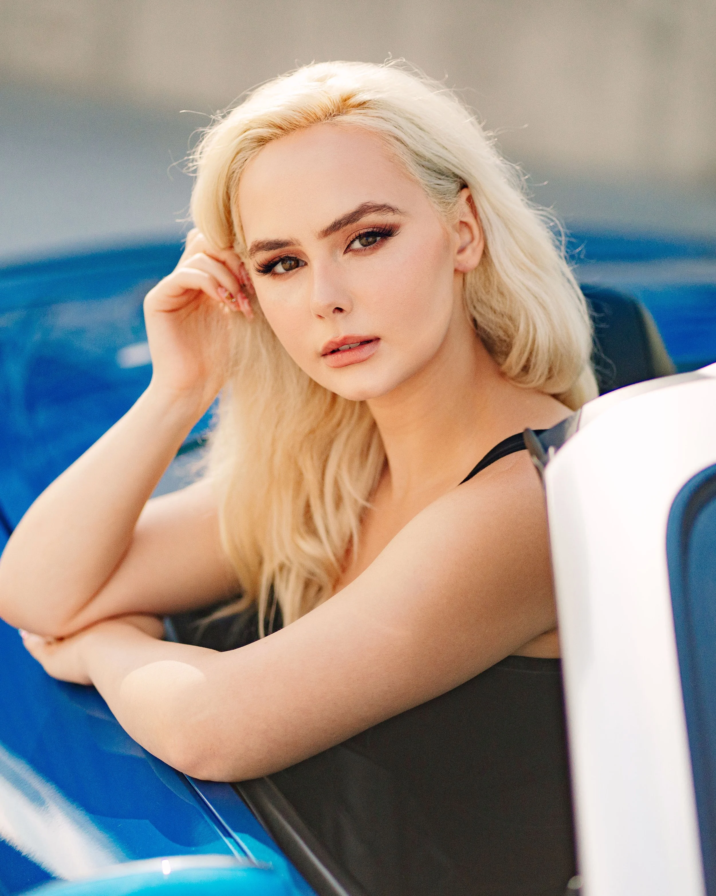 Atlanta Georgia professional headshots, A young woman with long blonde hair and makeup resting her arm on the window of a blue convertible car, looking at the camera.