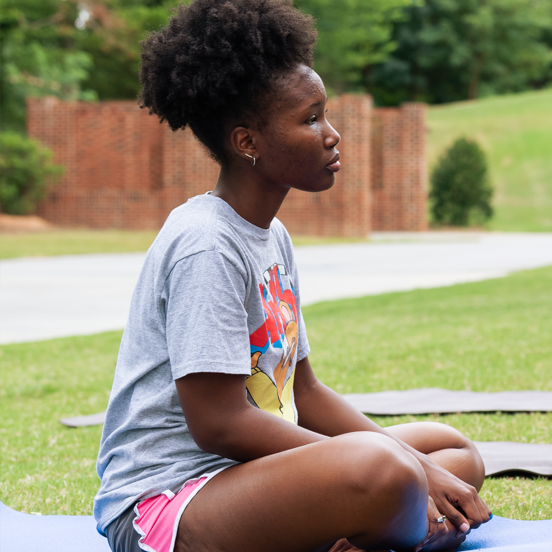 A peer staffer sits on a yoga mat, criss-crossed, and looks ahead.