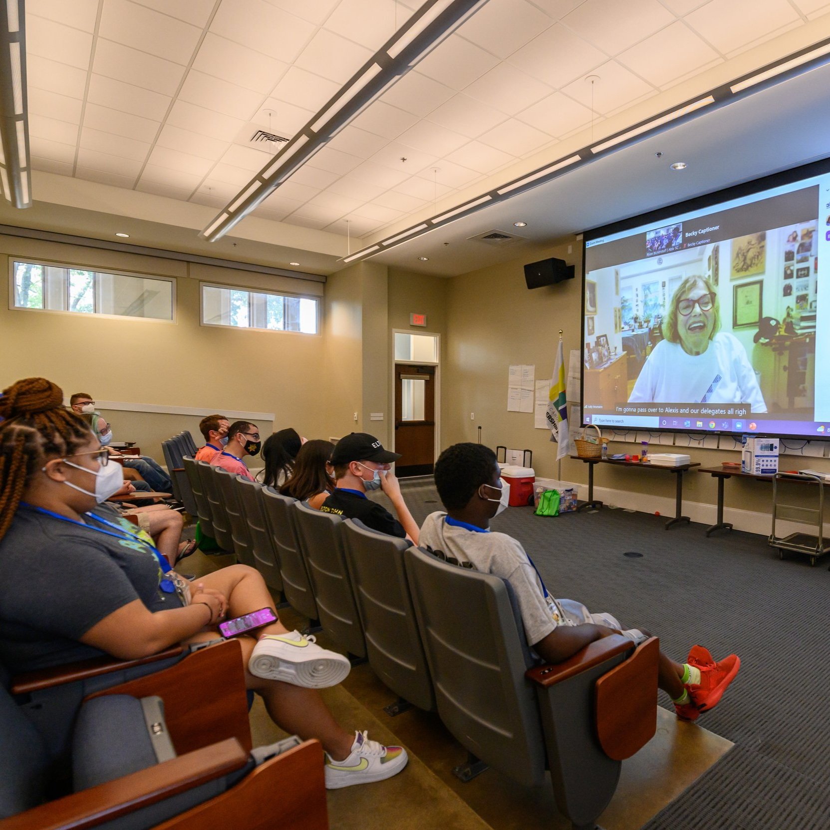 Internationally famous disability rights activist, Judy Huemann, speaks to the delegates via zoom, projected on a screen to a full classroom.