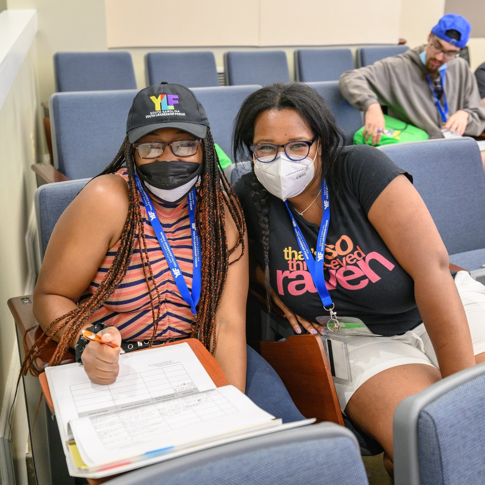 YLF delegate and YLF staffer smile behind facemasks while seated in the classroom.