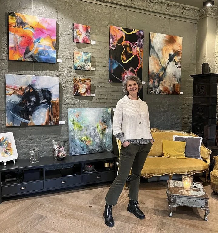 Gro Moe i galleri omgitt av fargerike abstrakte malerier, gul sofa og rustikt bord