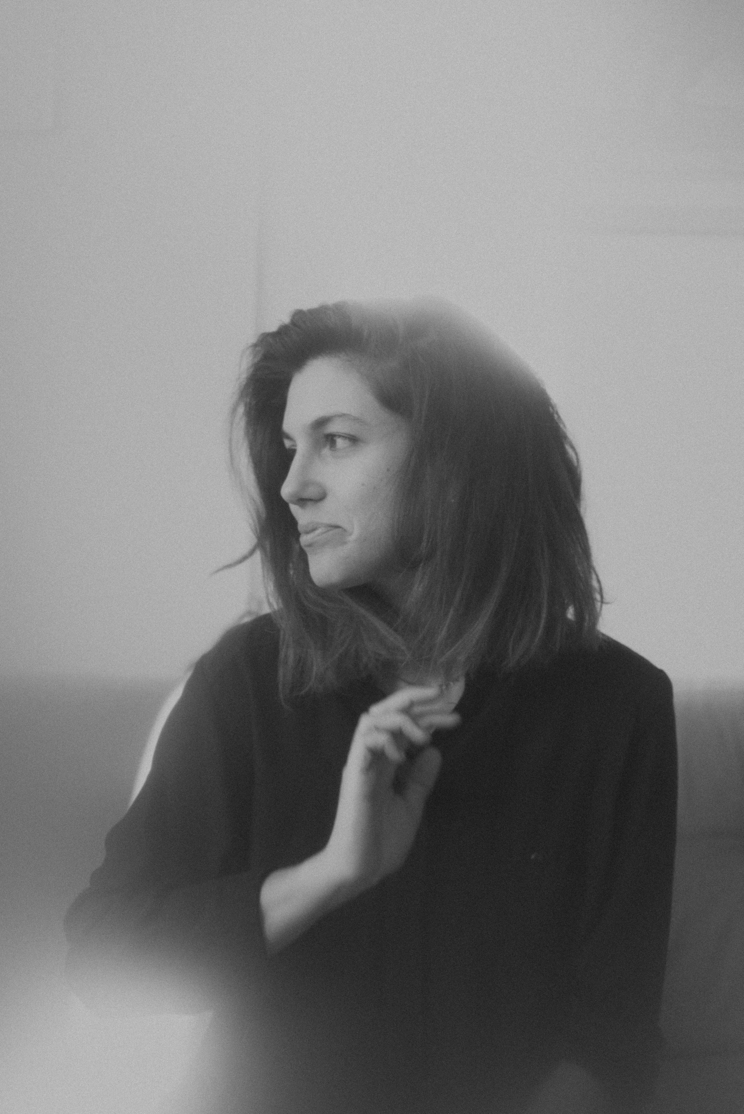 Black and white photo of a woman with long hair, wearing a dark top, touching her chin and looking sideways.
