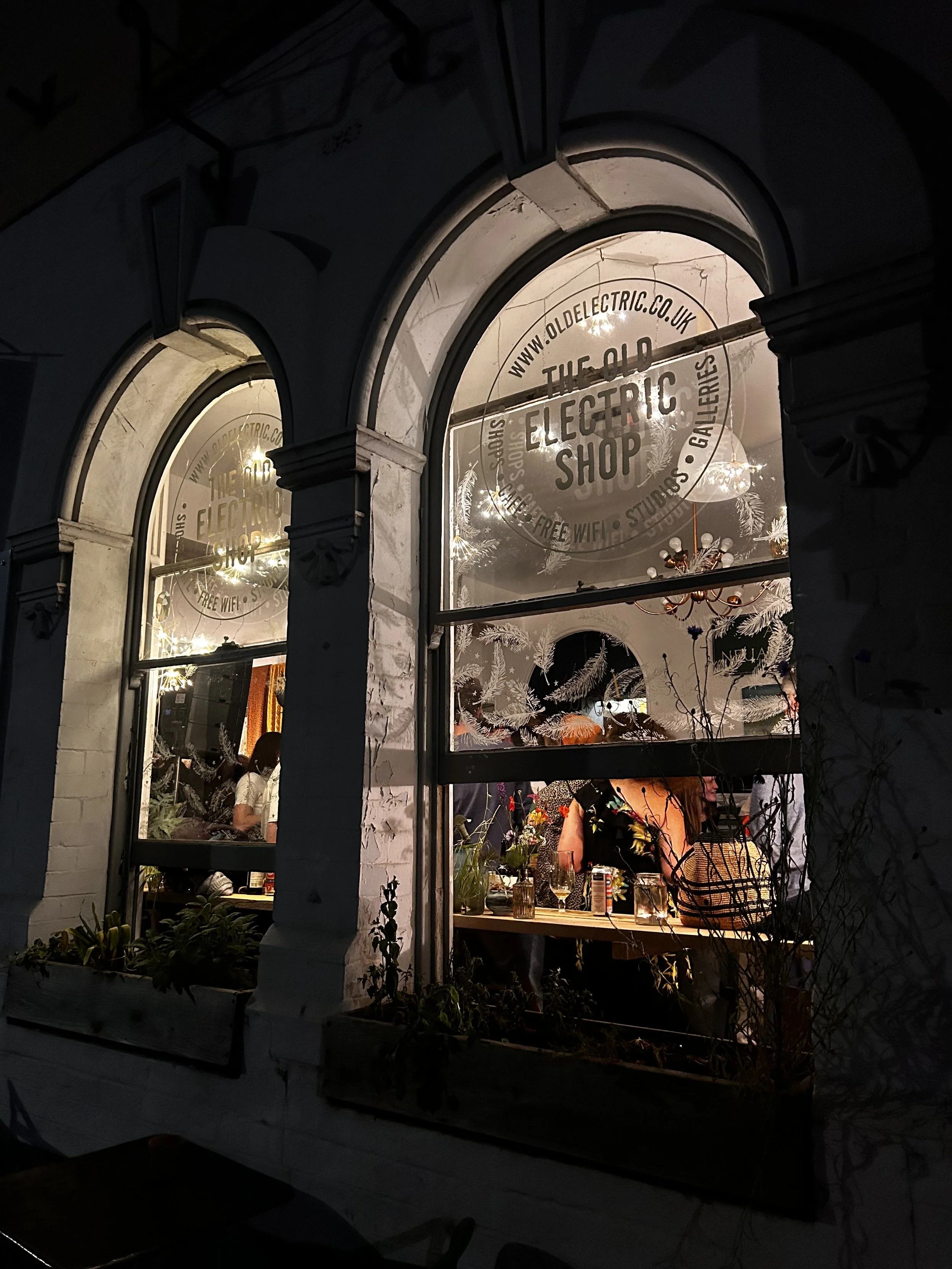 The shop front at night with large arched windows, during an event at The Old Electric Shop in Hay-on-Wye.
