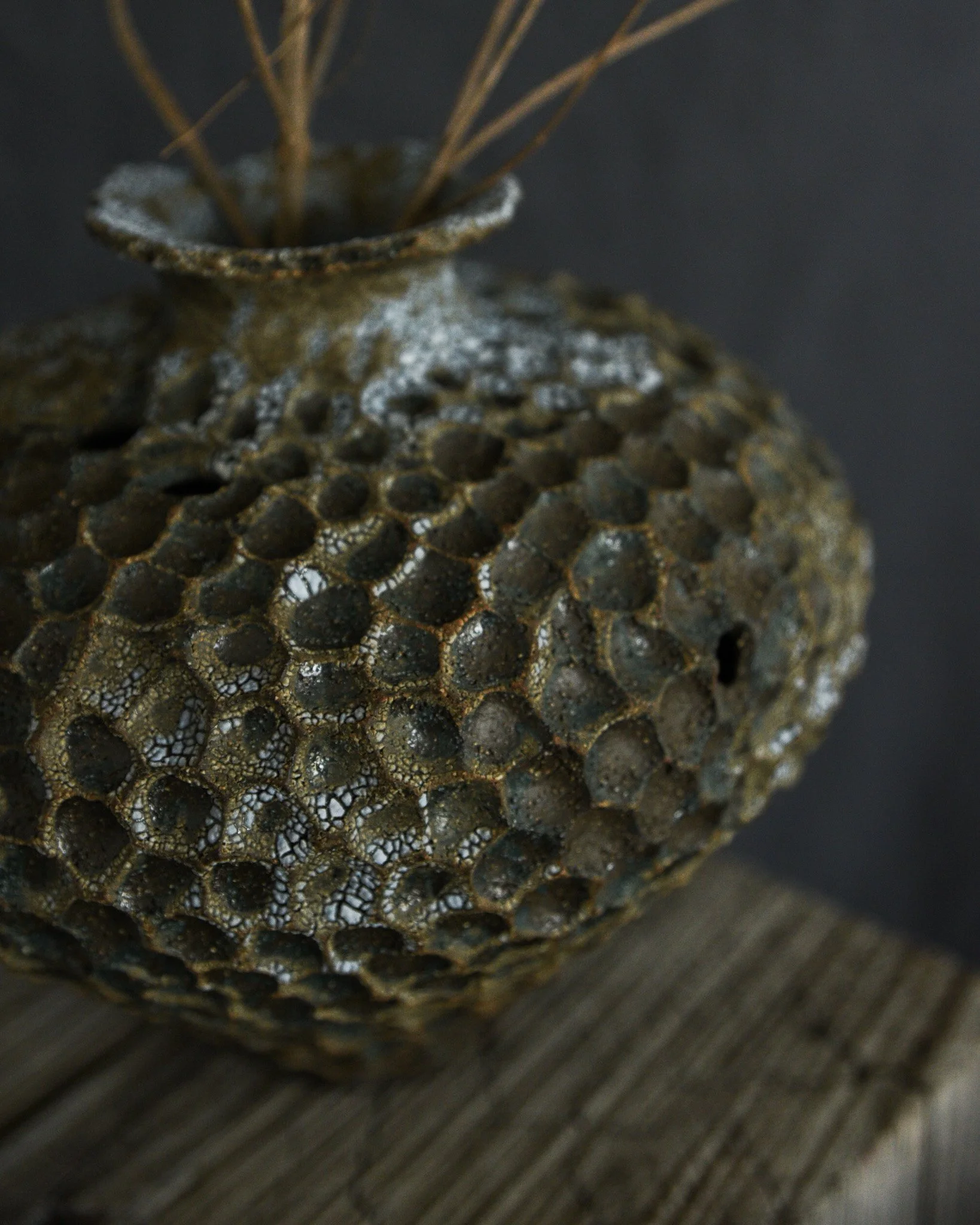 Close-up of a textured, honeycomb-patterned ceramic or stone object with thin metal rods protruding from the top, placed on a wooden surface.