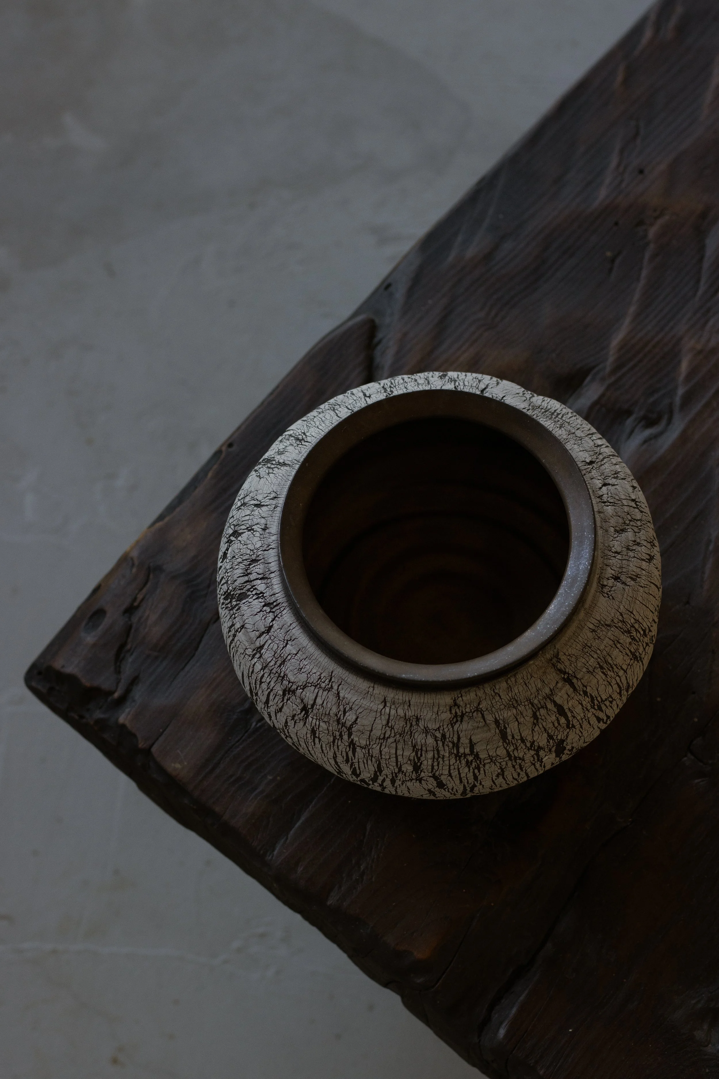 Close-up view of a vintage ceramic vessel with a cracked, distressed finish, placed on a rustic wooden surface.