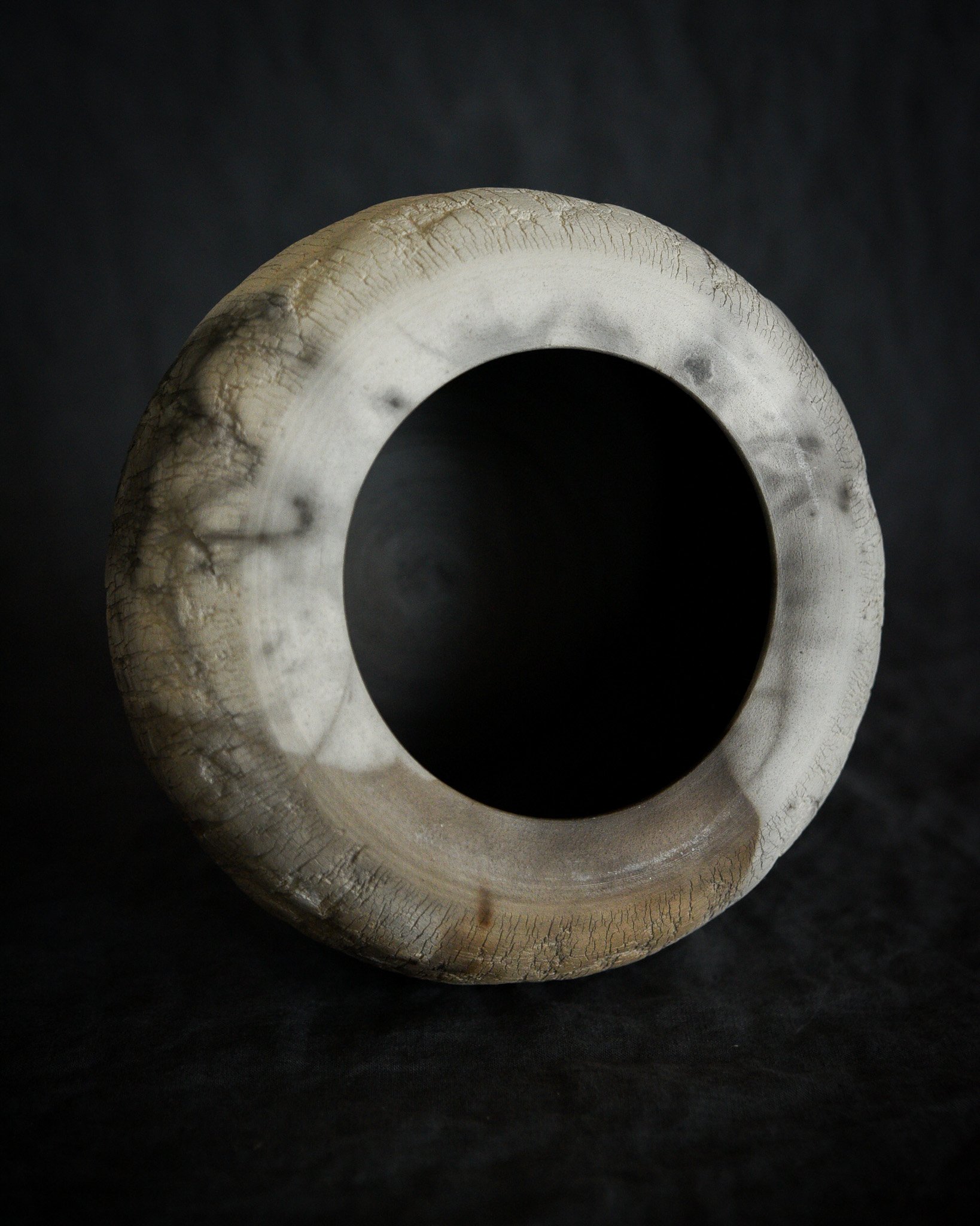 Close-up of a hollow, round, white ceramic or stone object with a large central hole, against a black background.