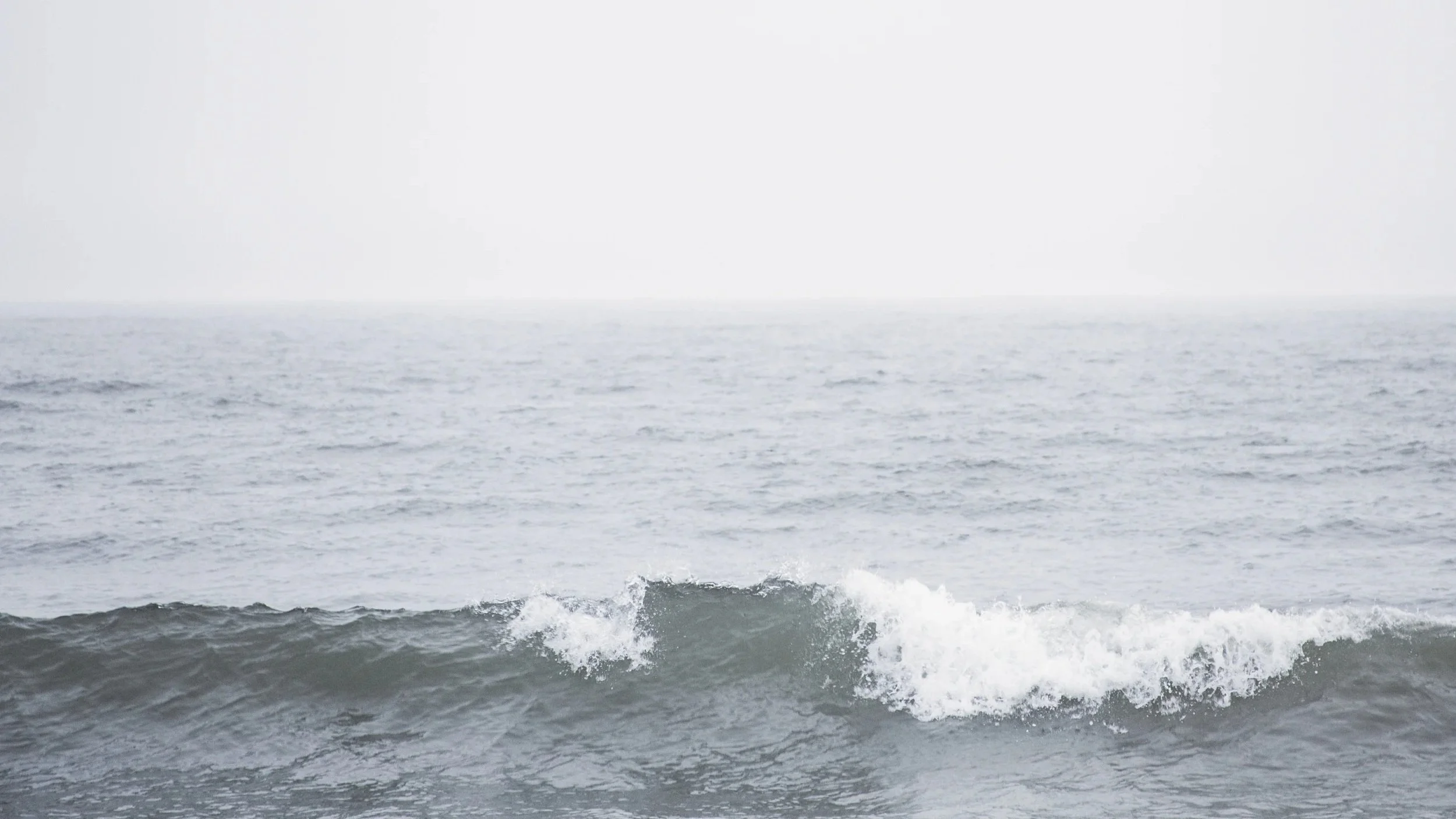A calm ocean with gentle waves and a foggy horizon.