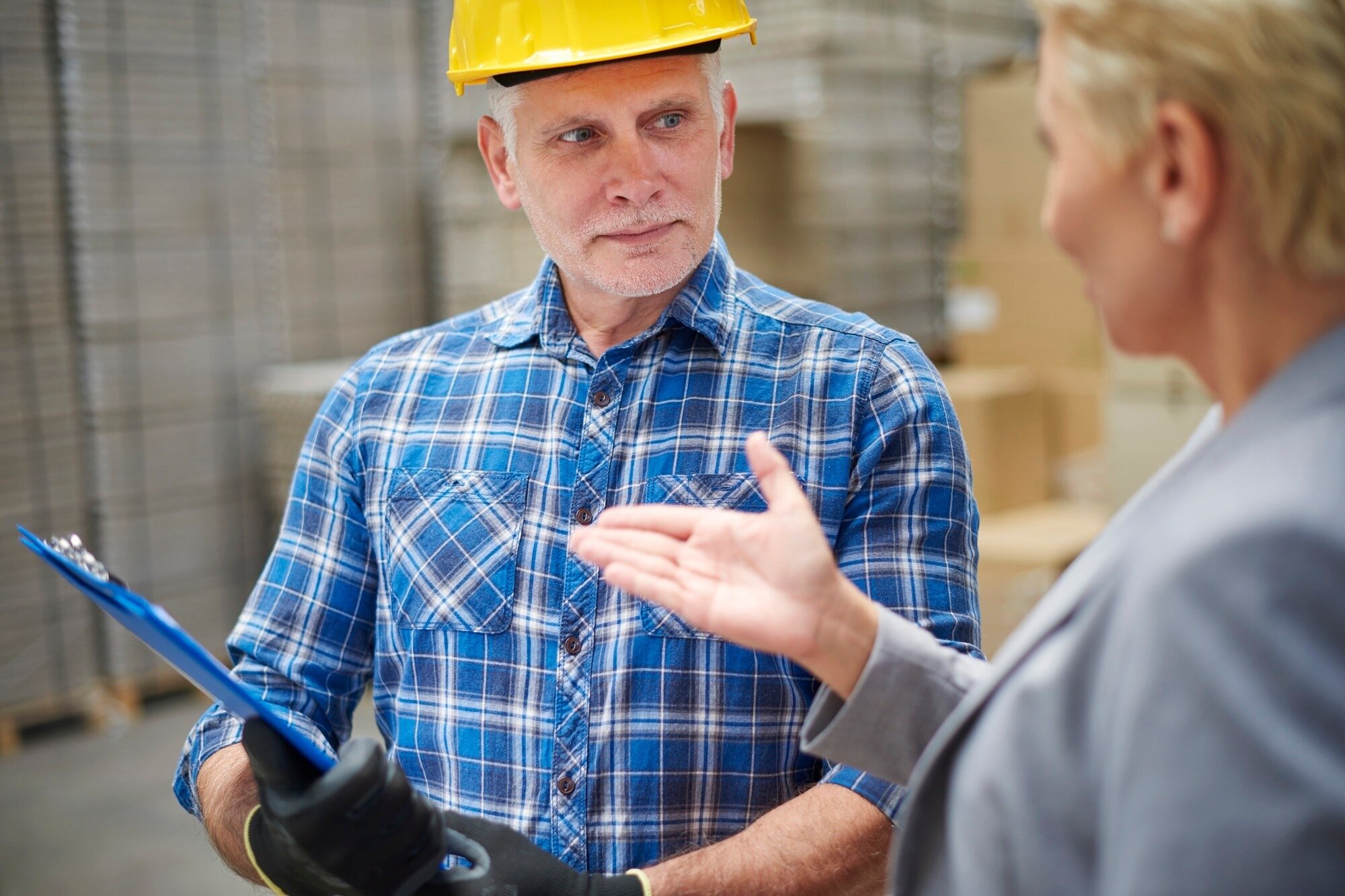A man and woman engaged in conversation inside a spacious warehouse filled with shelves and boxes