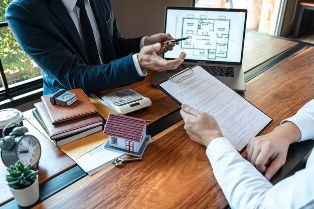 Two men in suits seated at a table, working with a laptop and papers in a professional setting