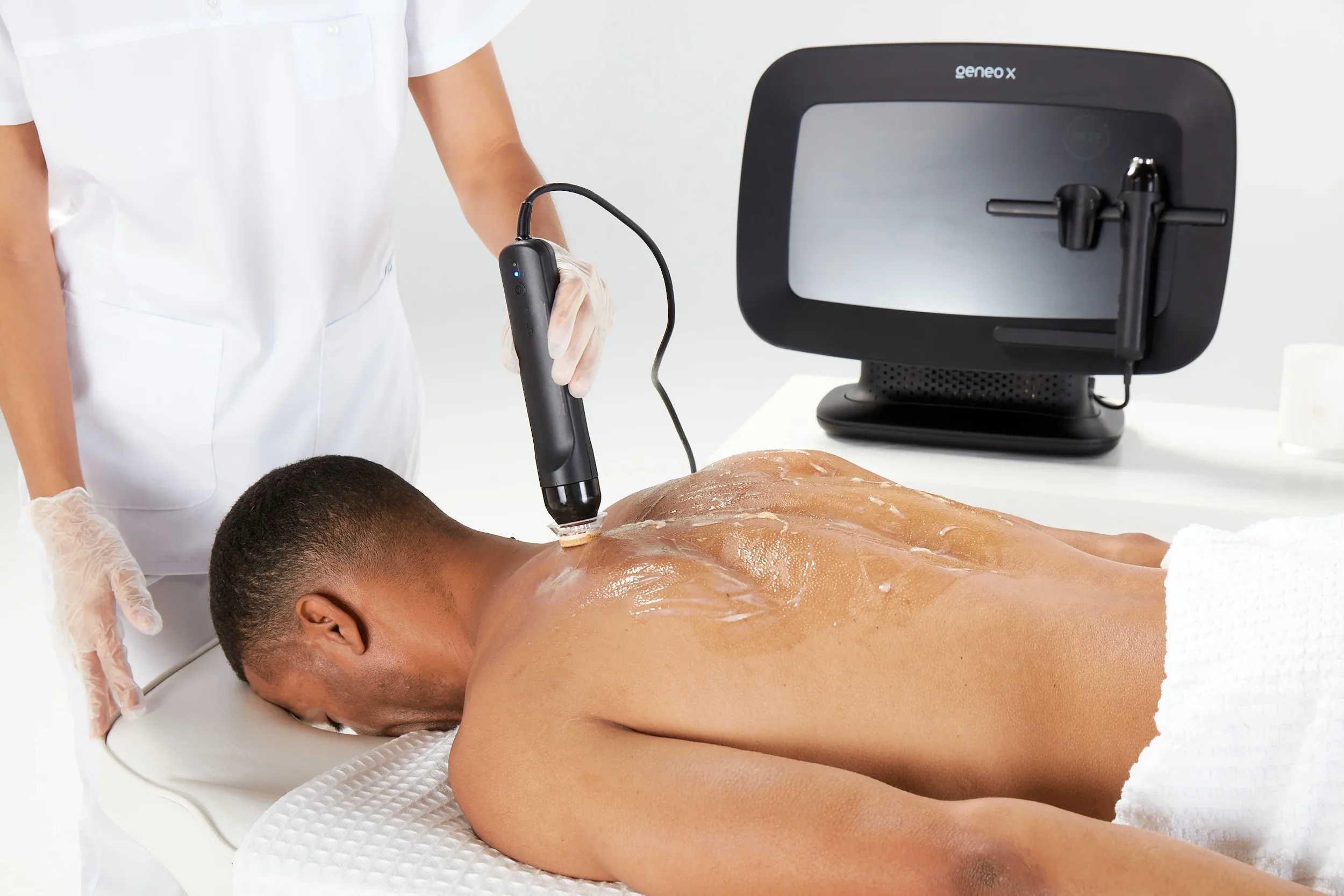 A person receiving a laser treatment on their back performed by a healthcare professional in a medical setting, with a laser device and monitor visible.