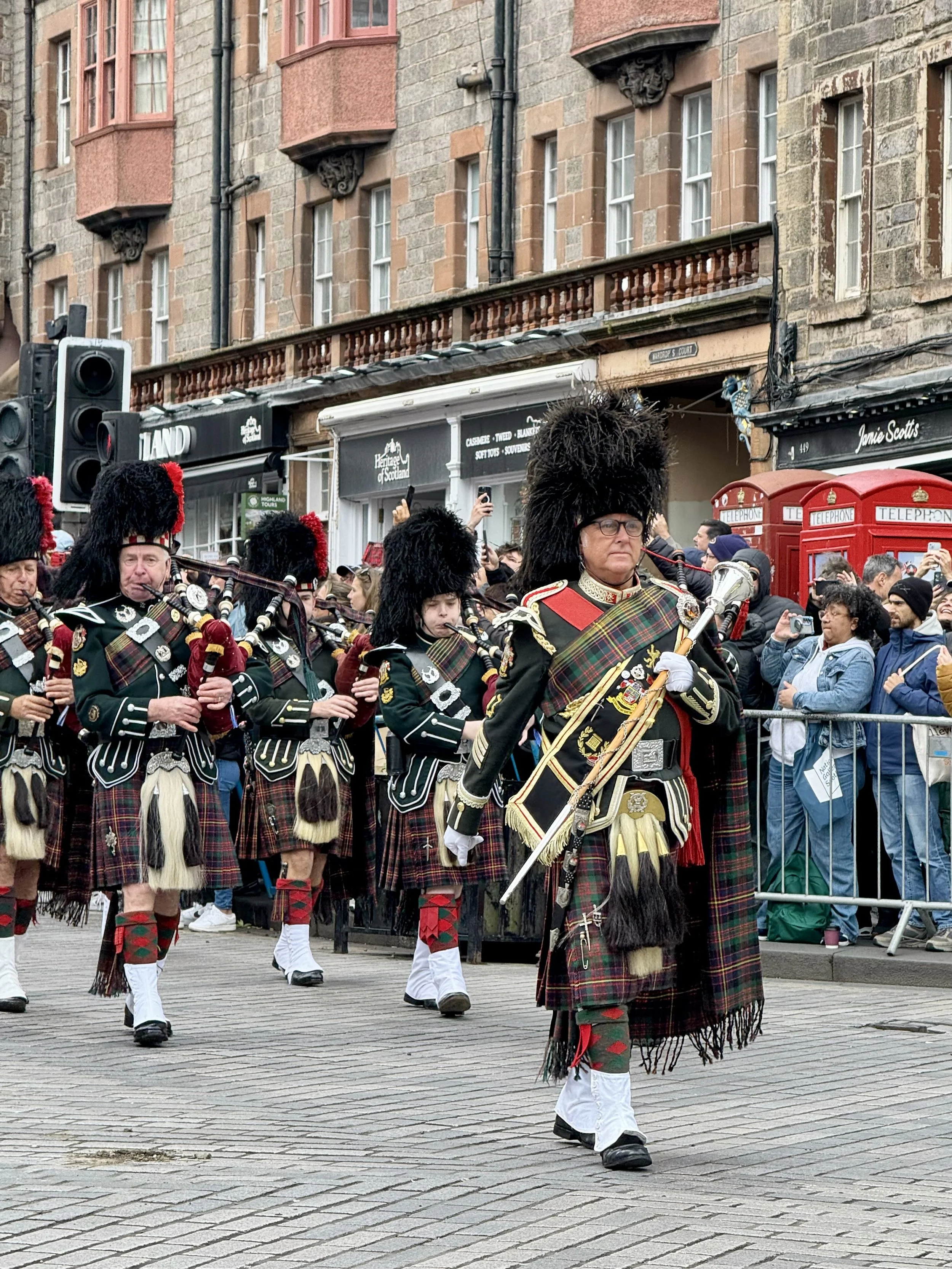 A Scottish bagpipe band wearing full tartan uniform and hats marching in the Edinburgh Tartan Parade