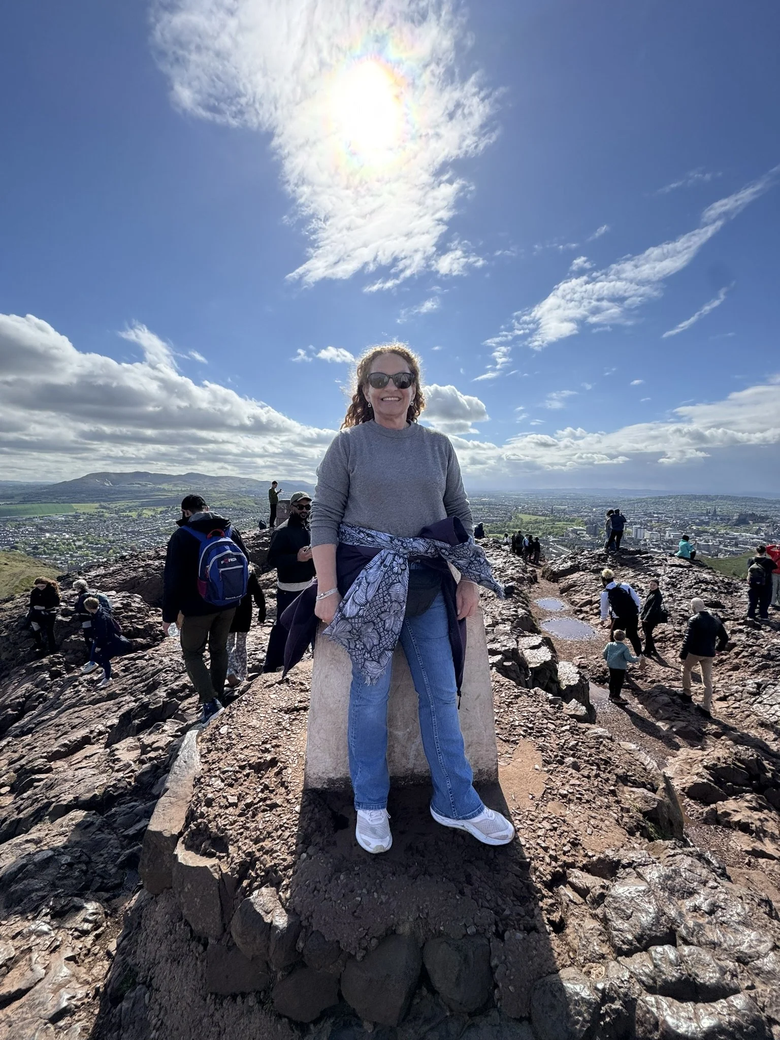 Woman stood on top of Arthurs Seat hill in Edinburgh with views of the city and countryside for miles