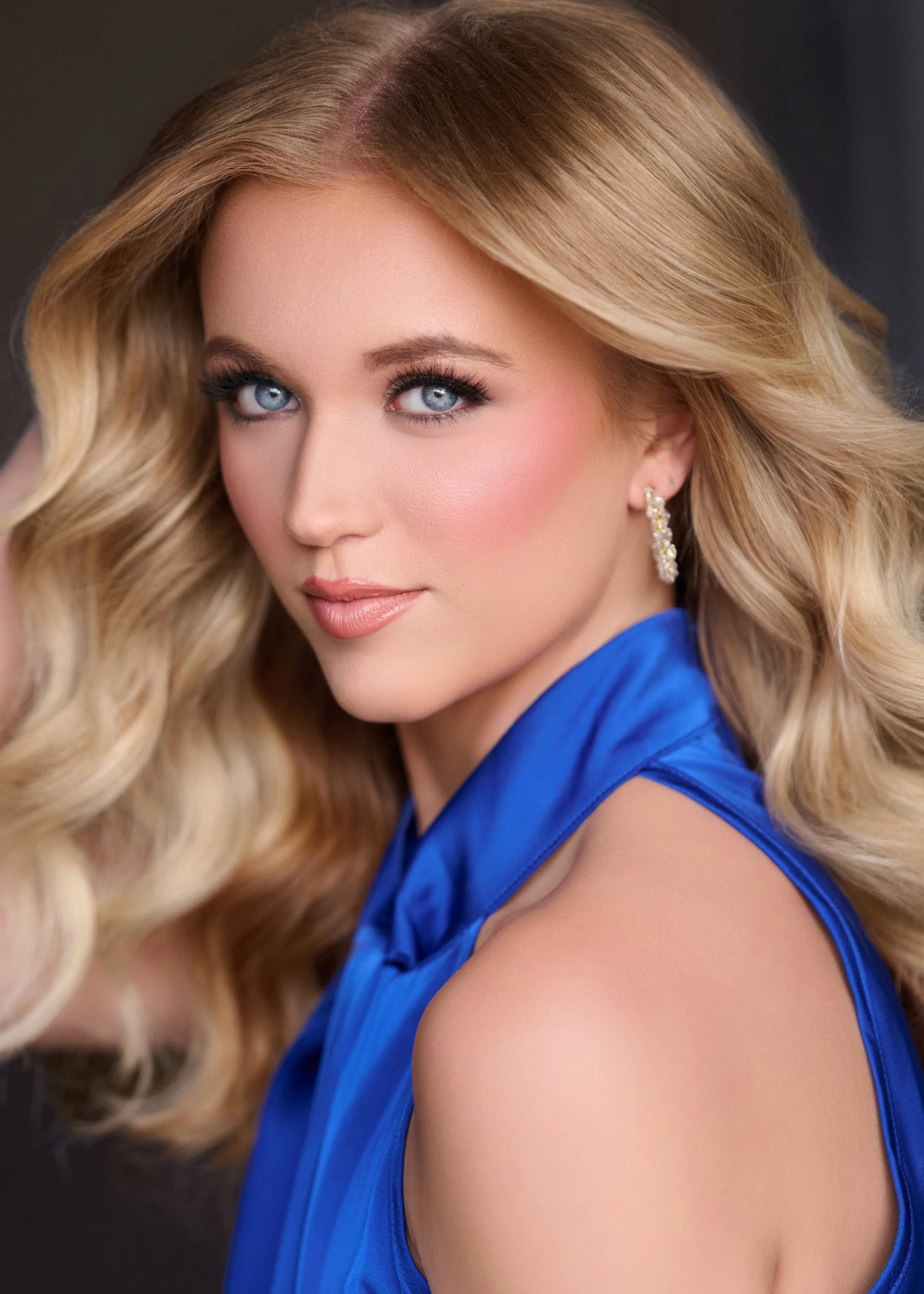 Smiling woman with long blonde hair, wearing a white top and hoop earrings.