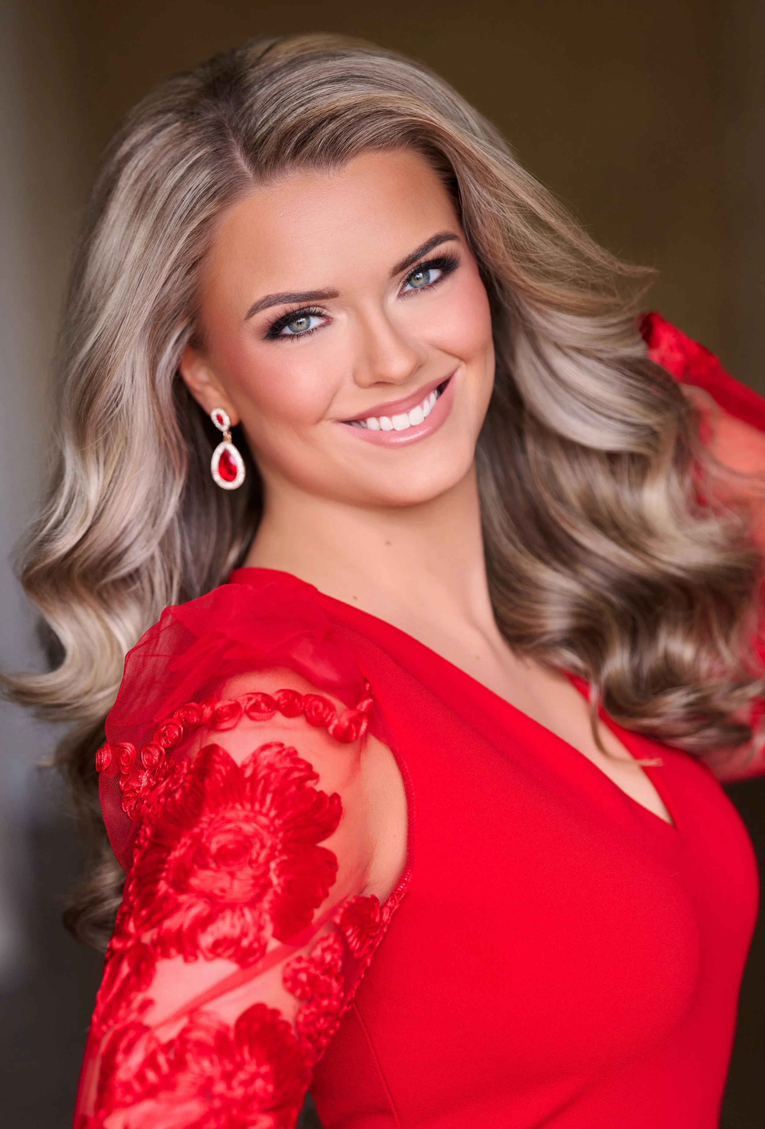 Smiling woman in a blue dress with short blonde hair and pearl earrings.