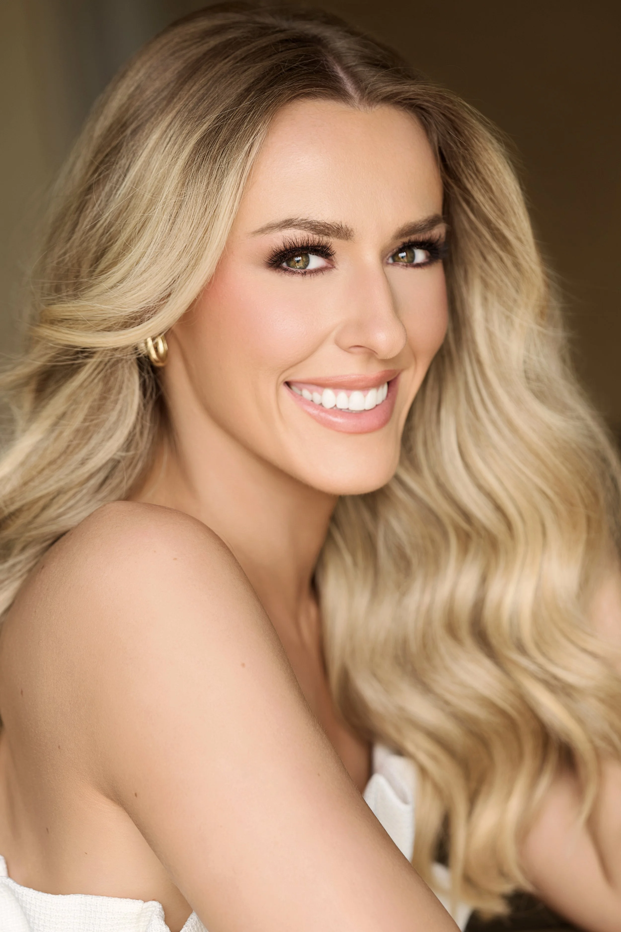 Smiling woman in a sparkly blue top with curly hair and blue earrings against a plain background.