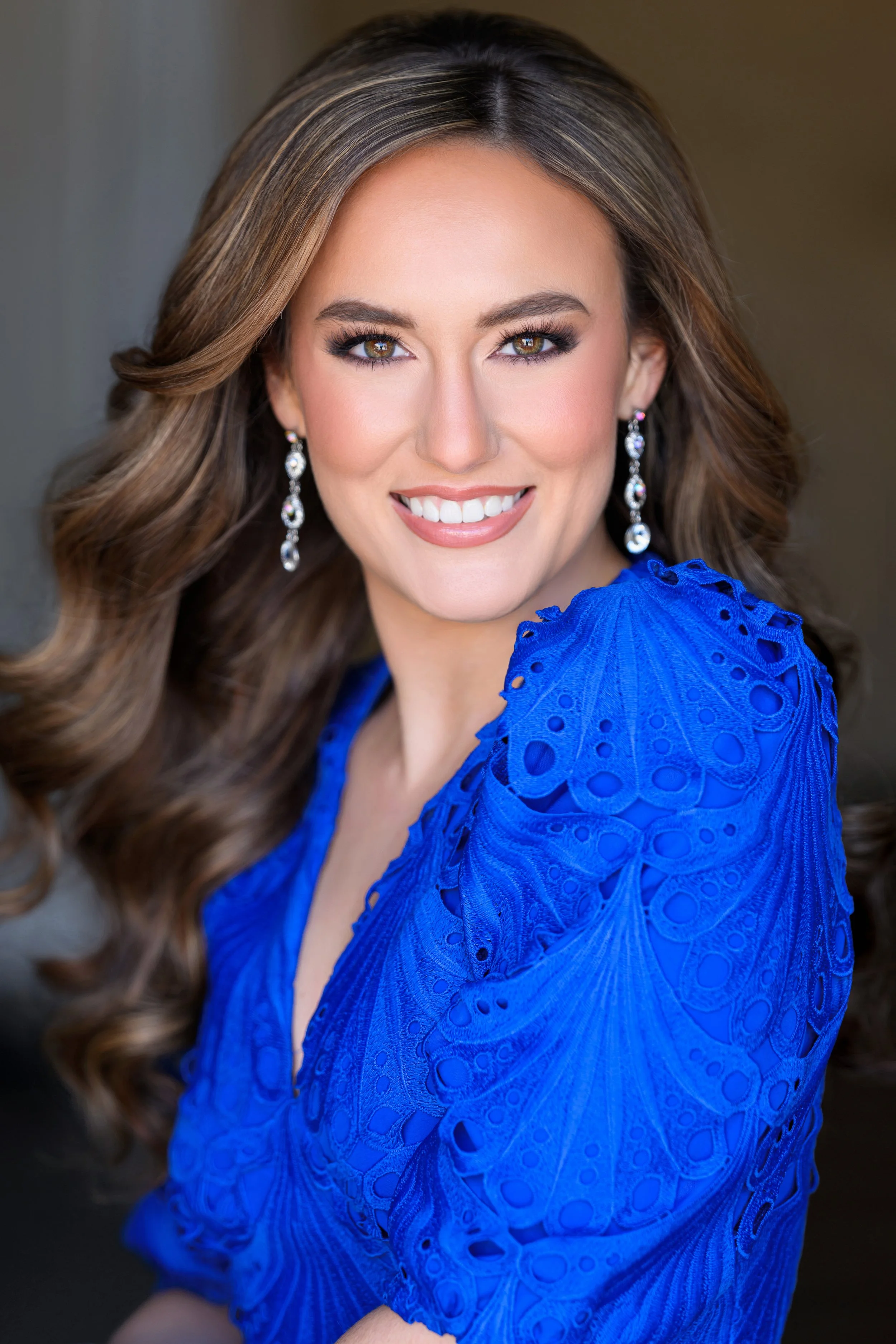 Portrait of a smiling woman with long blonde hair and wearing a red dress against a dark background.