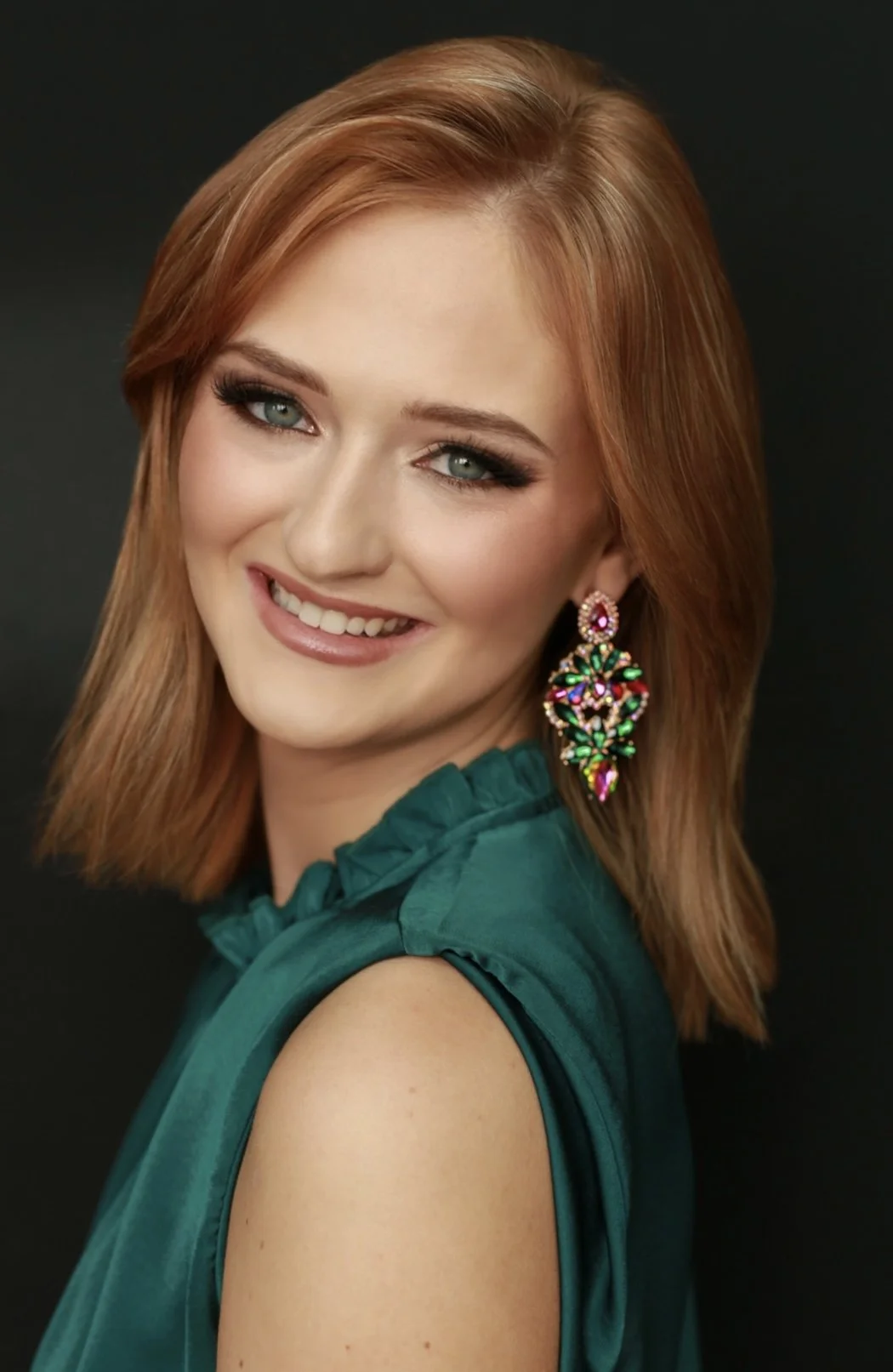 Woman in a green dress smiling with wavy brown hair and statement earrings.