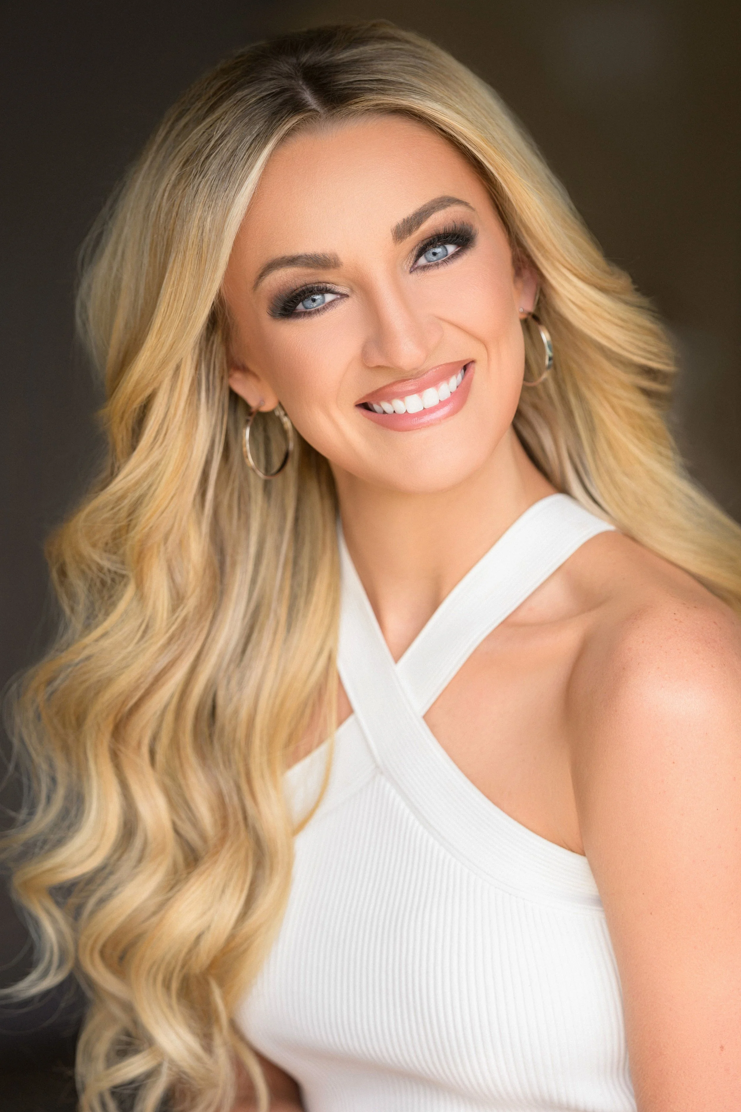 Smiling woman with long blonde hair, wearing blue earrings and a blue dress.