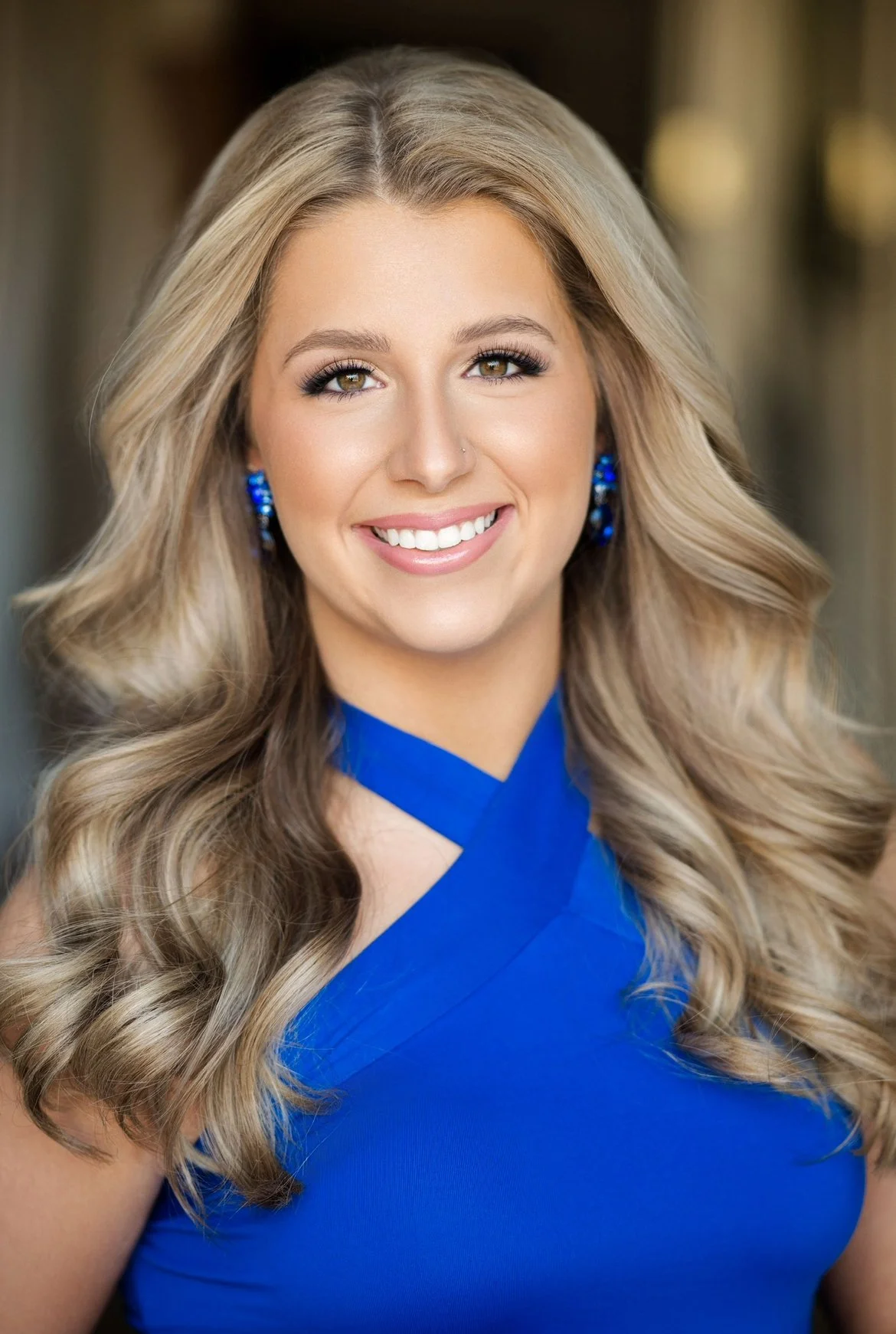 Smiling woman with long blonde hair, wearing blue earrings and a blue dress.