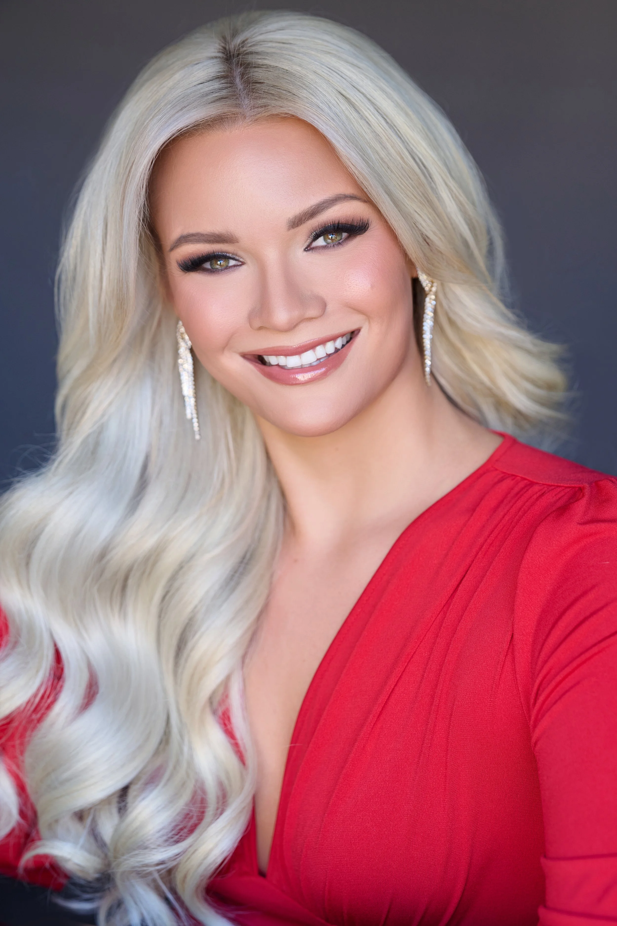Woman with brown hair wearing a blue dress and earrings, smiling.