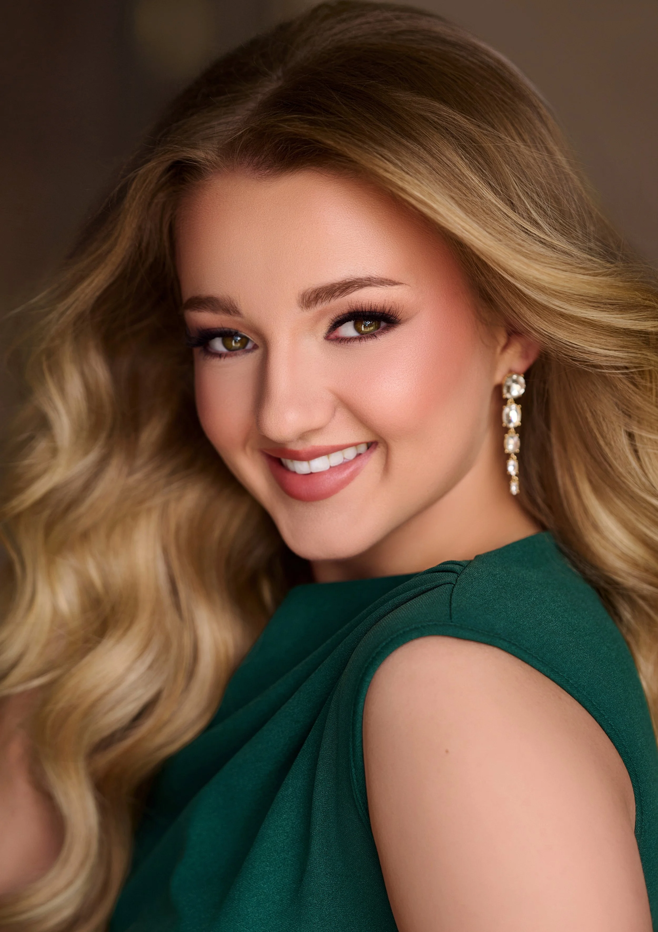 A person with long, curly hair smiling, wearing a blue top and earrings.