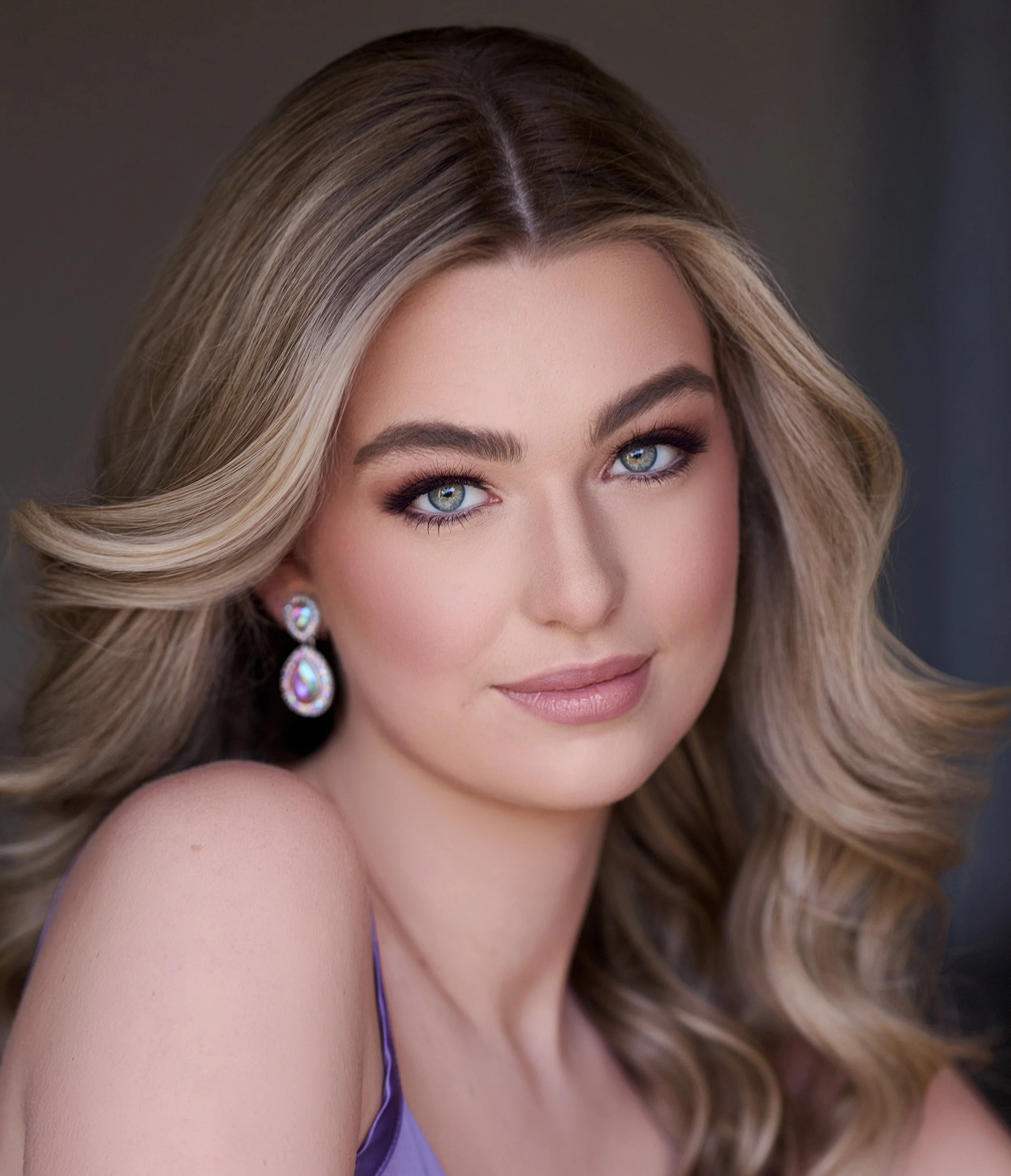 Smiling woman with long brown hair wearing a green top and earrings