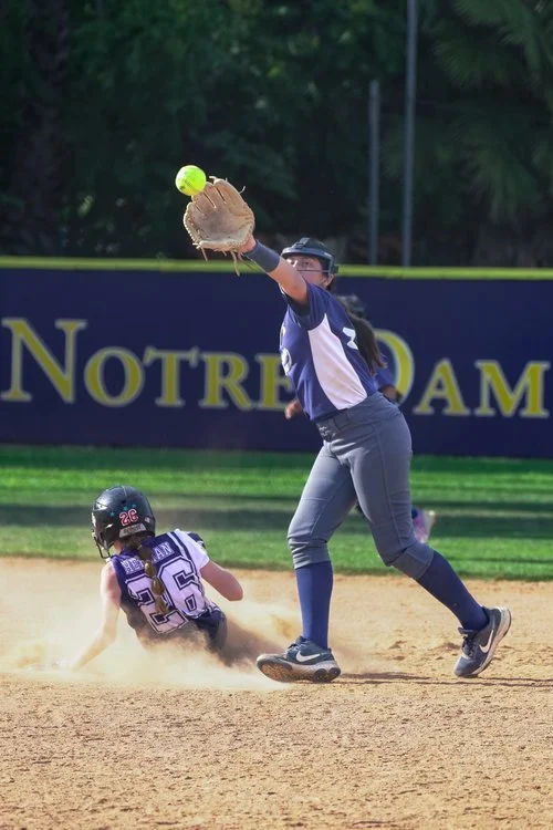 Softball players making a play catching the ball as a player slides in the dirt