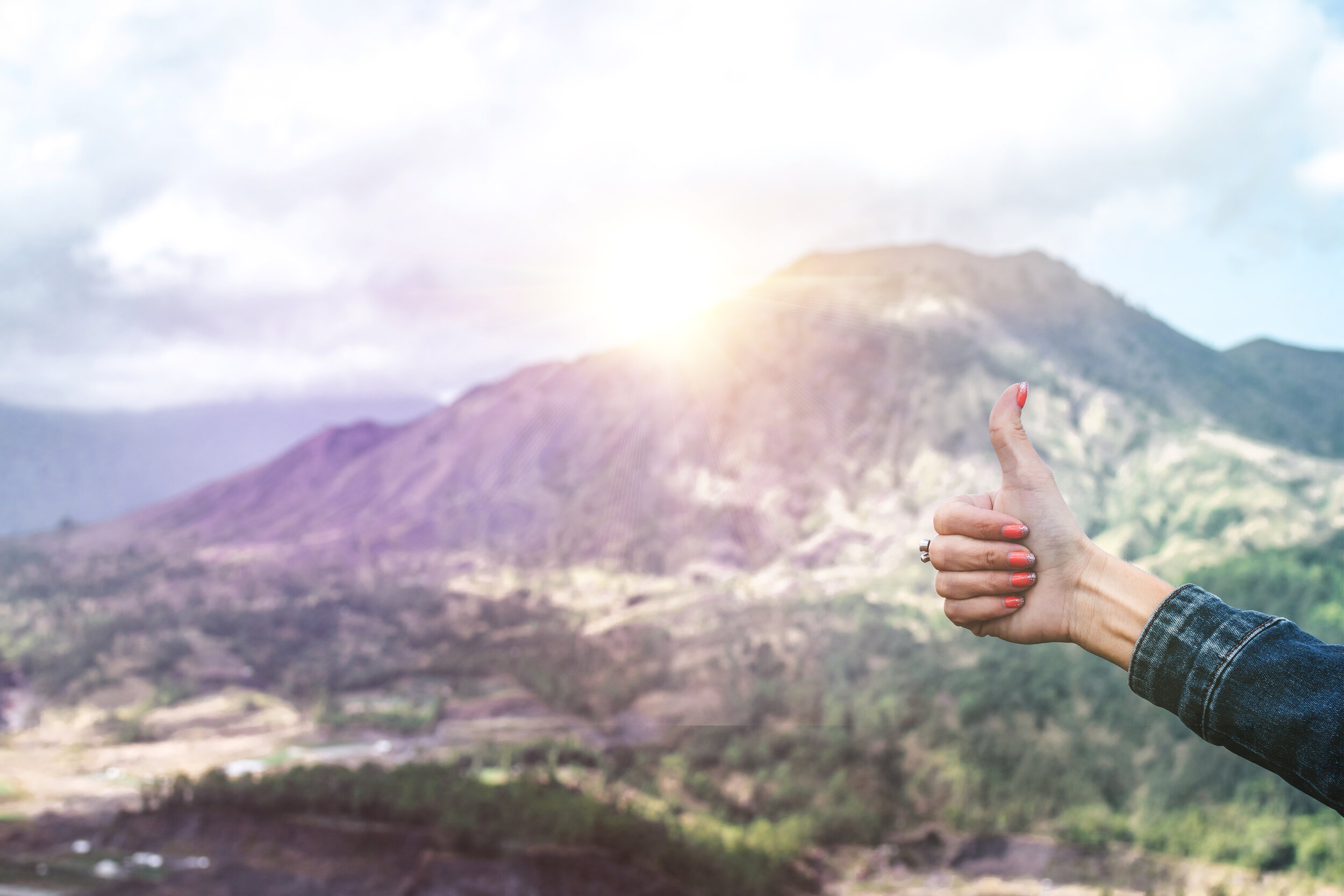 sunset over mountains with a woman giving a thumbs up