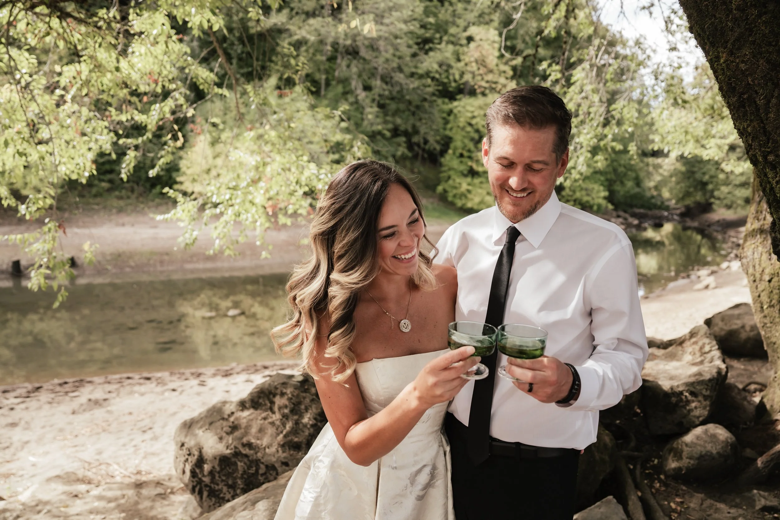 A happy couple smiles as they enjoy a beverage in a green glass along the banks of a river in Portland.