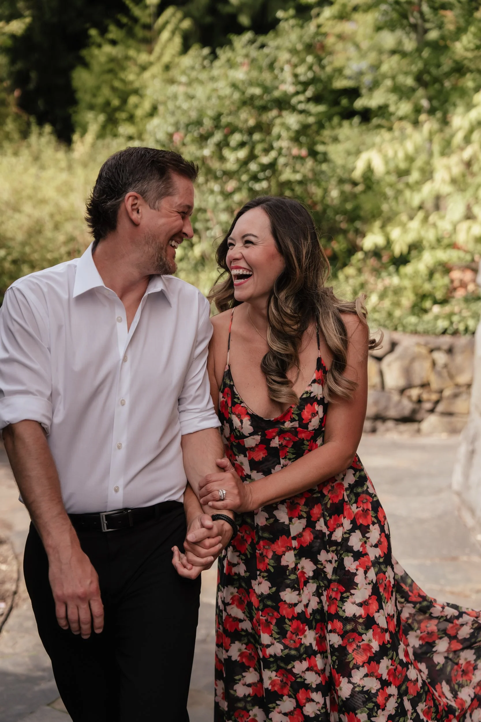A married couple laugh at each other as they grab arms and walk forward.
