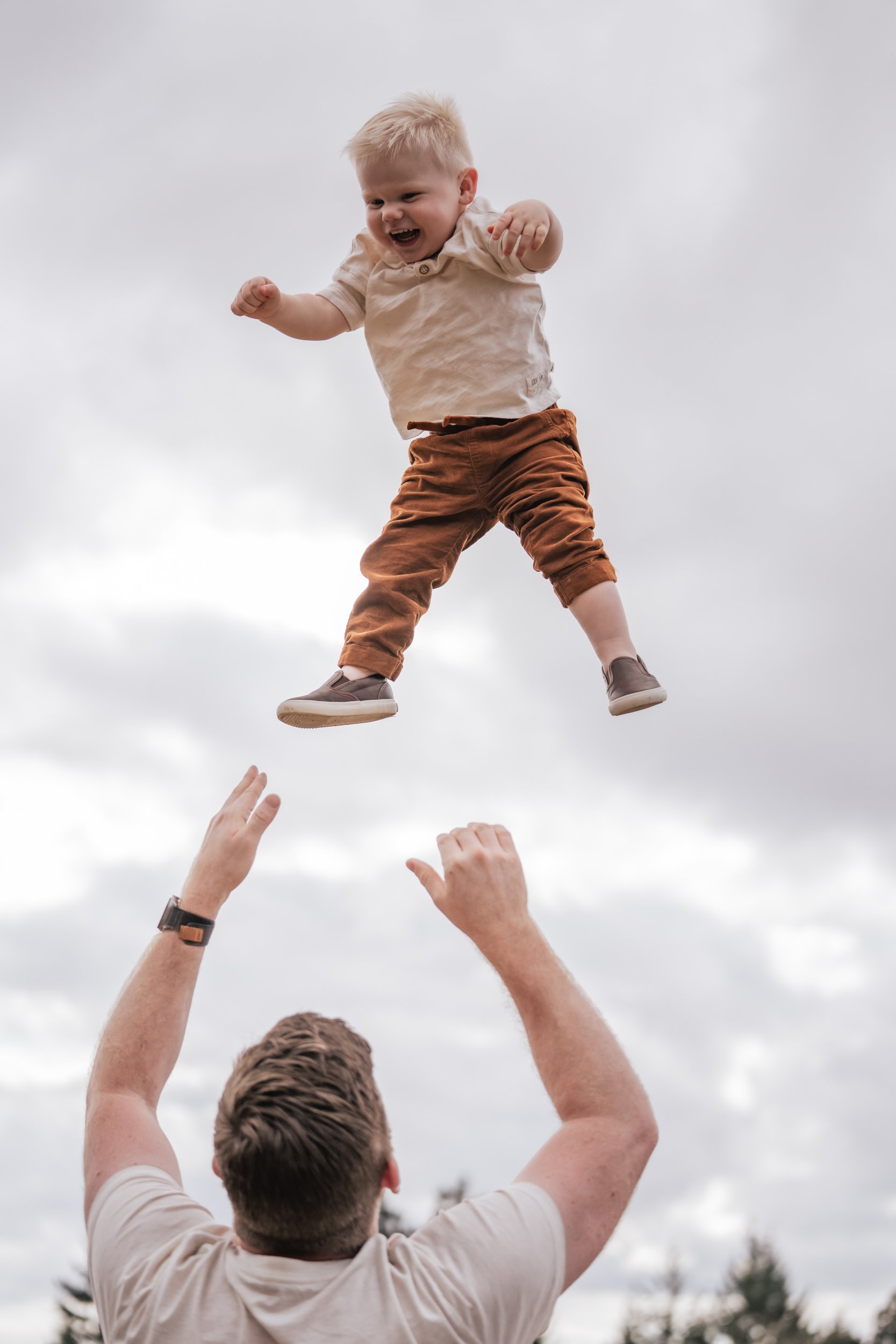A dad playfully launches his son into the air.