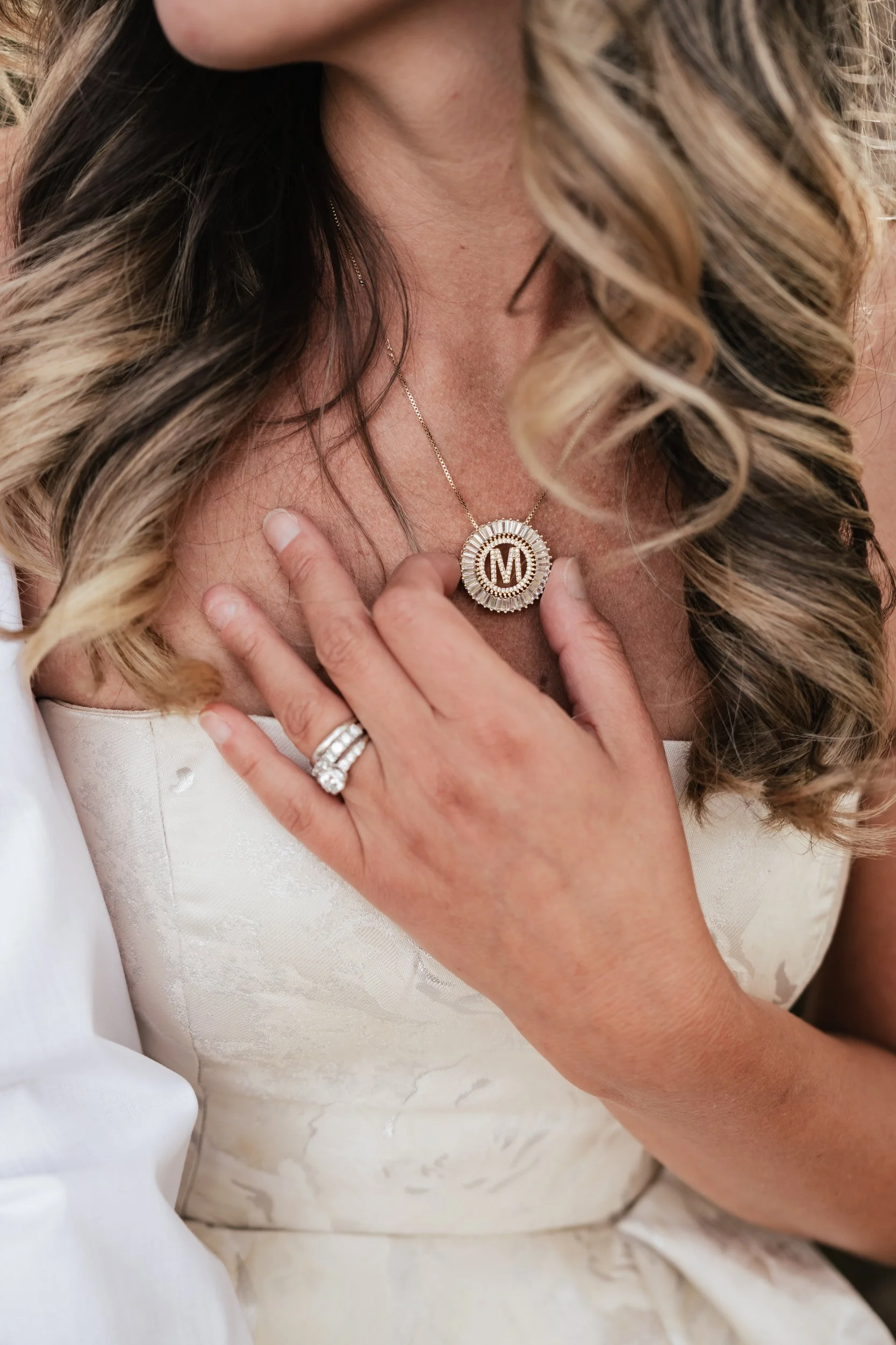 A woman with curly highlighted hair adjusts her gold diamond necklace.