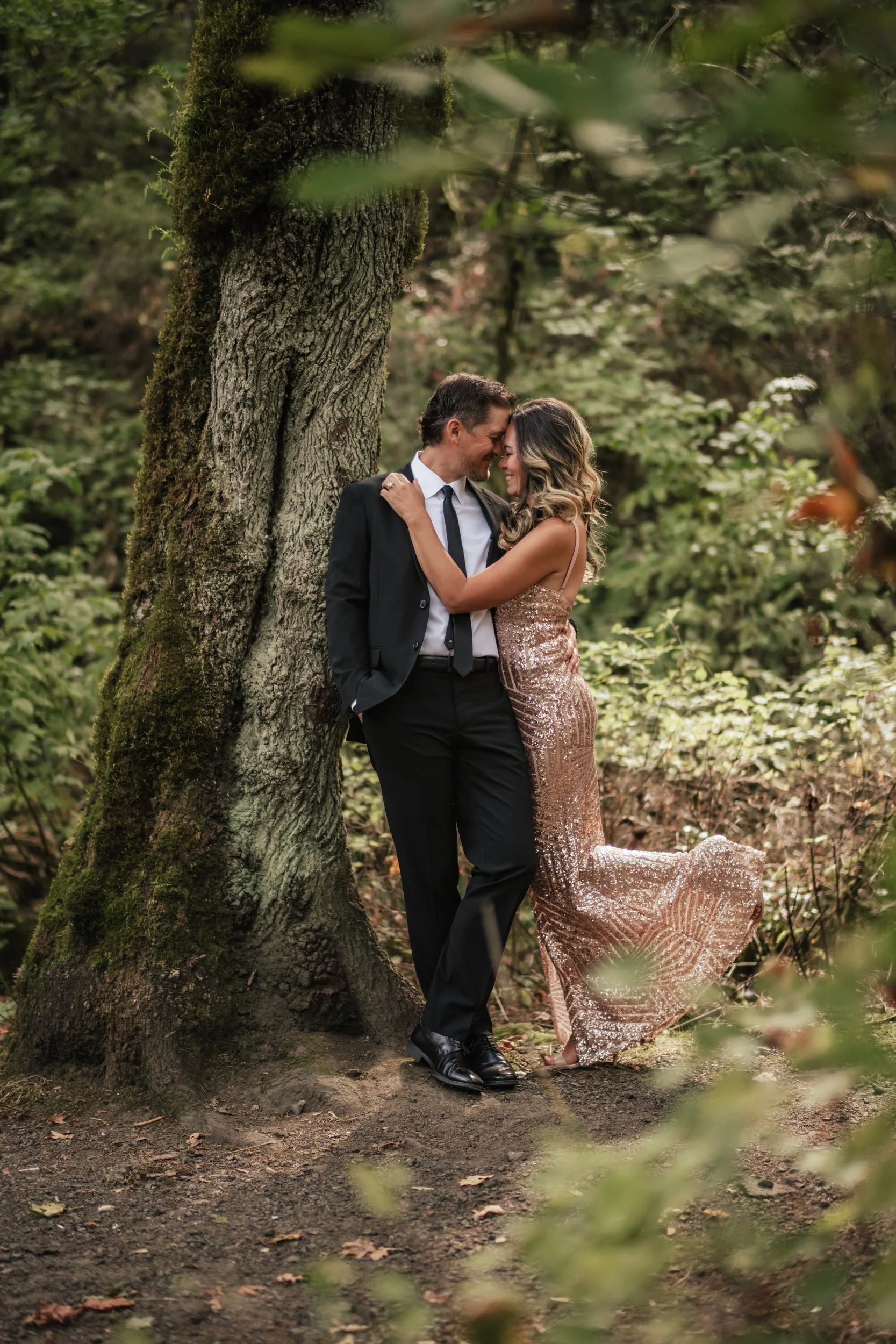 A woman in a beautiful dress lifts her leg to seductively kiss her man in a forest.