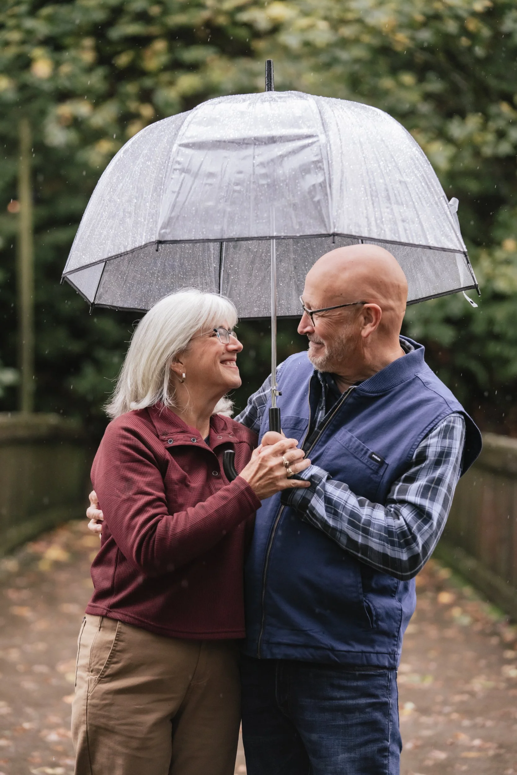 An older couple share a clear umbrella during a rainy day.