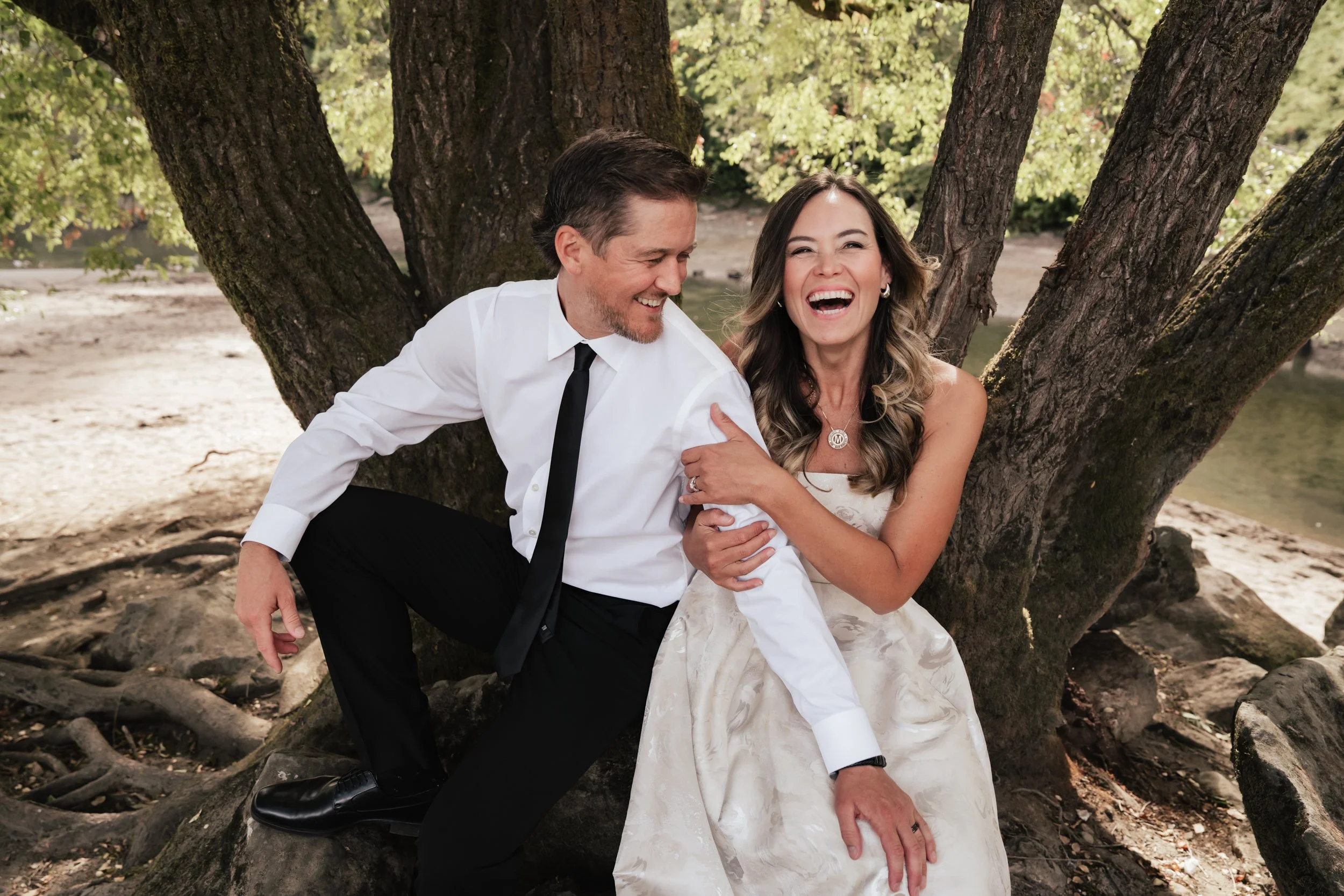 A woman grabs the arm of her date as they laugh in front of a tree.