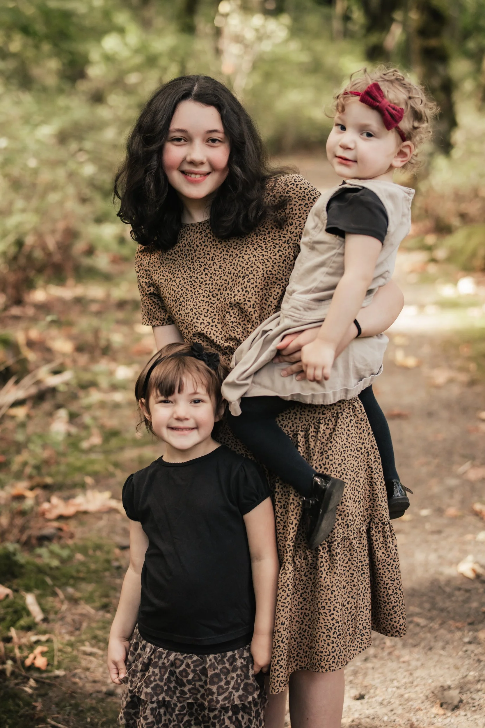 Three sisters pose together in a forested scene.