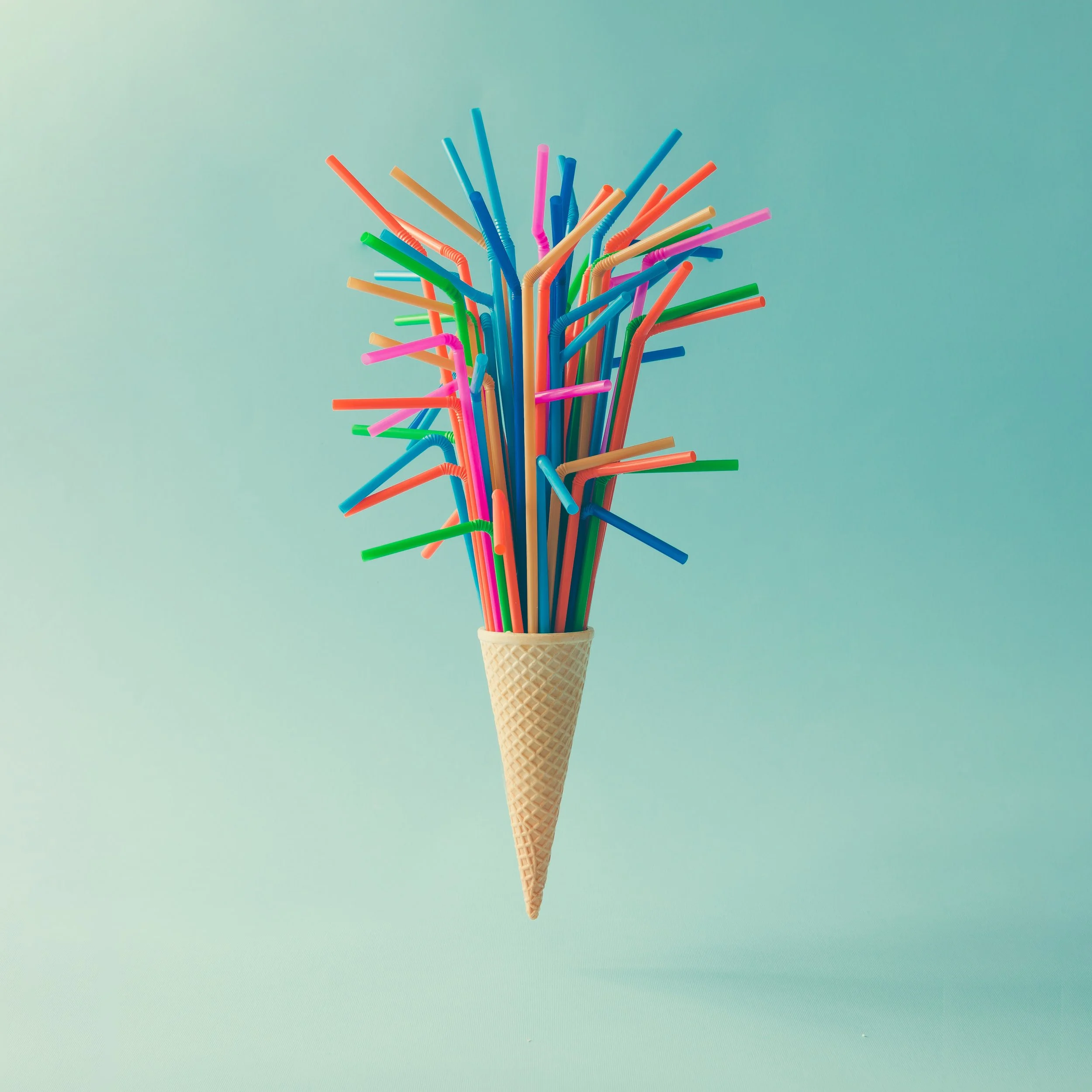 A bright blue ice cream cone with a waffle pattern, placed on a colorful yellow and green stand against a pink background.