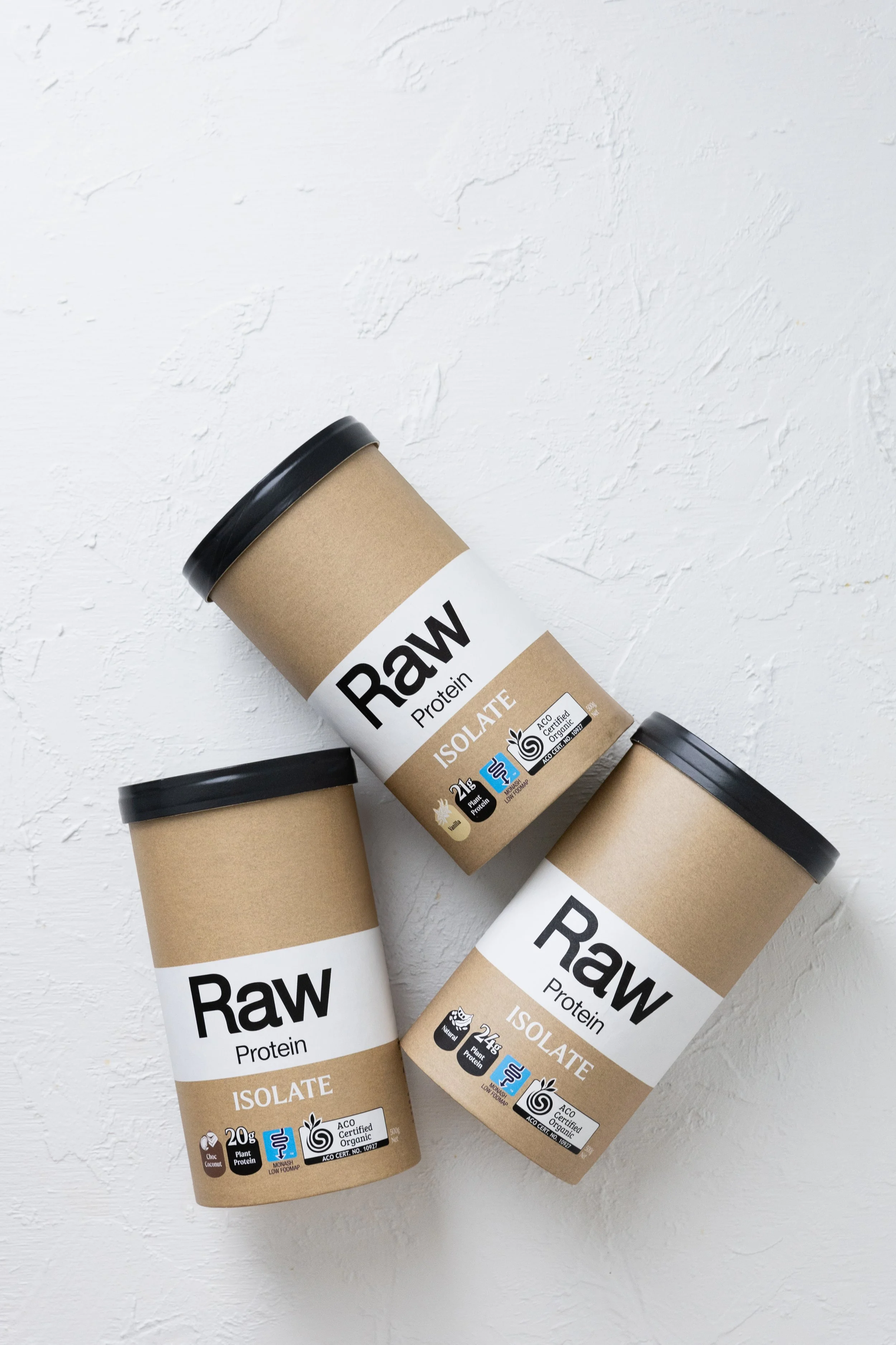 Three containers of Raw vegan protein isolate powder with black lids on a white textured surface.