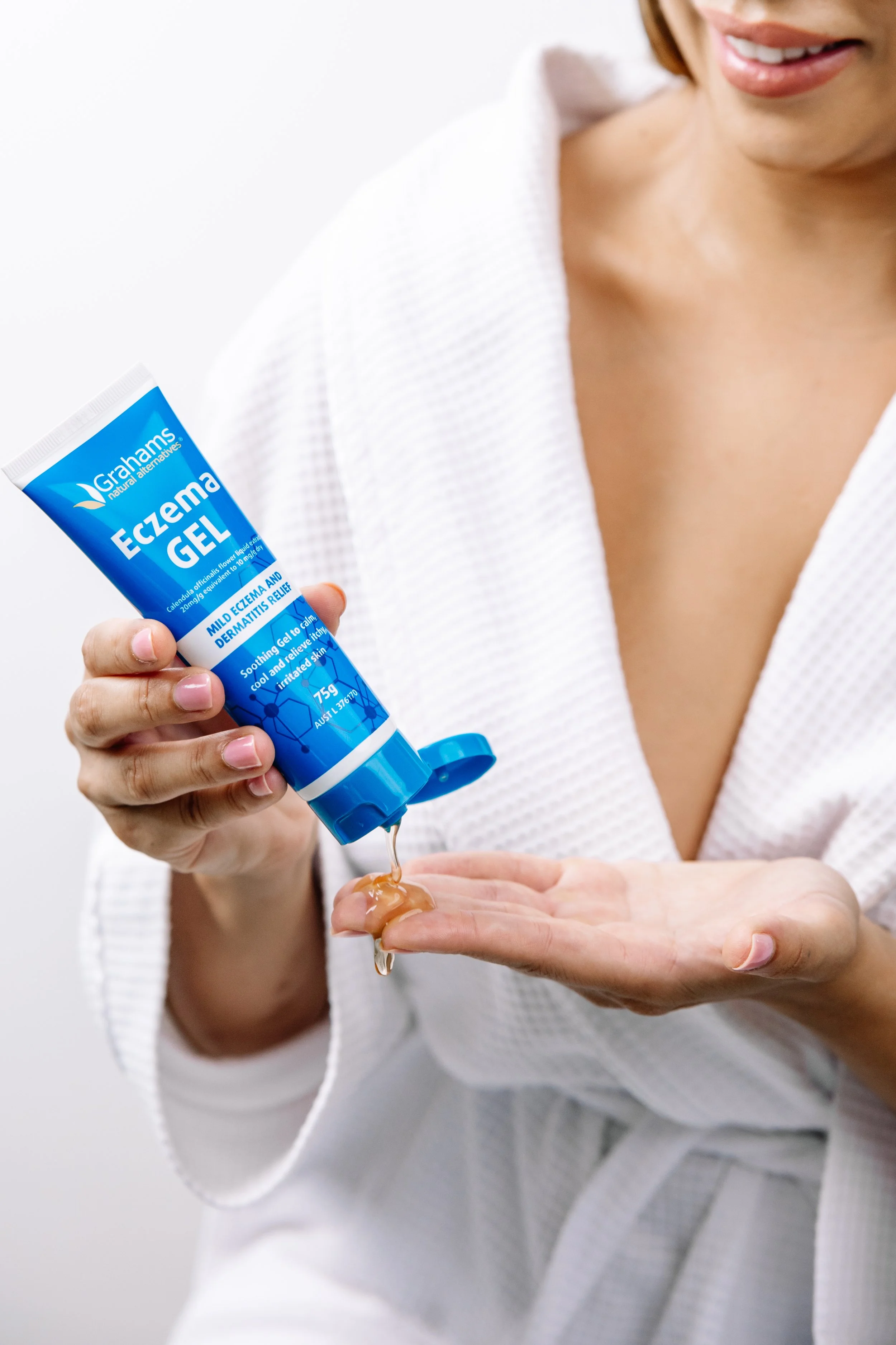 Woman in a white bathrobe squeezing eczema relief gel onto her hand.