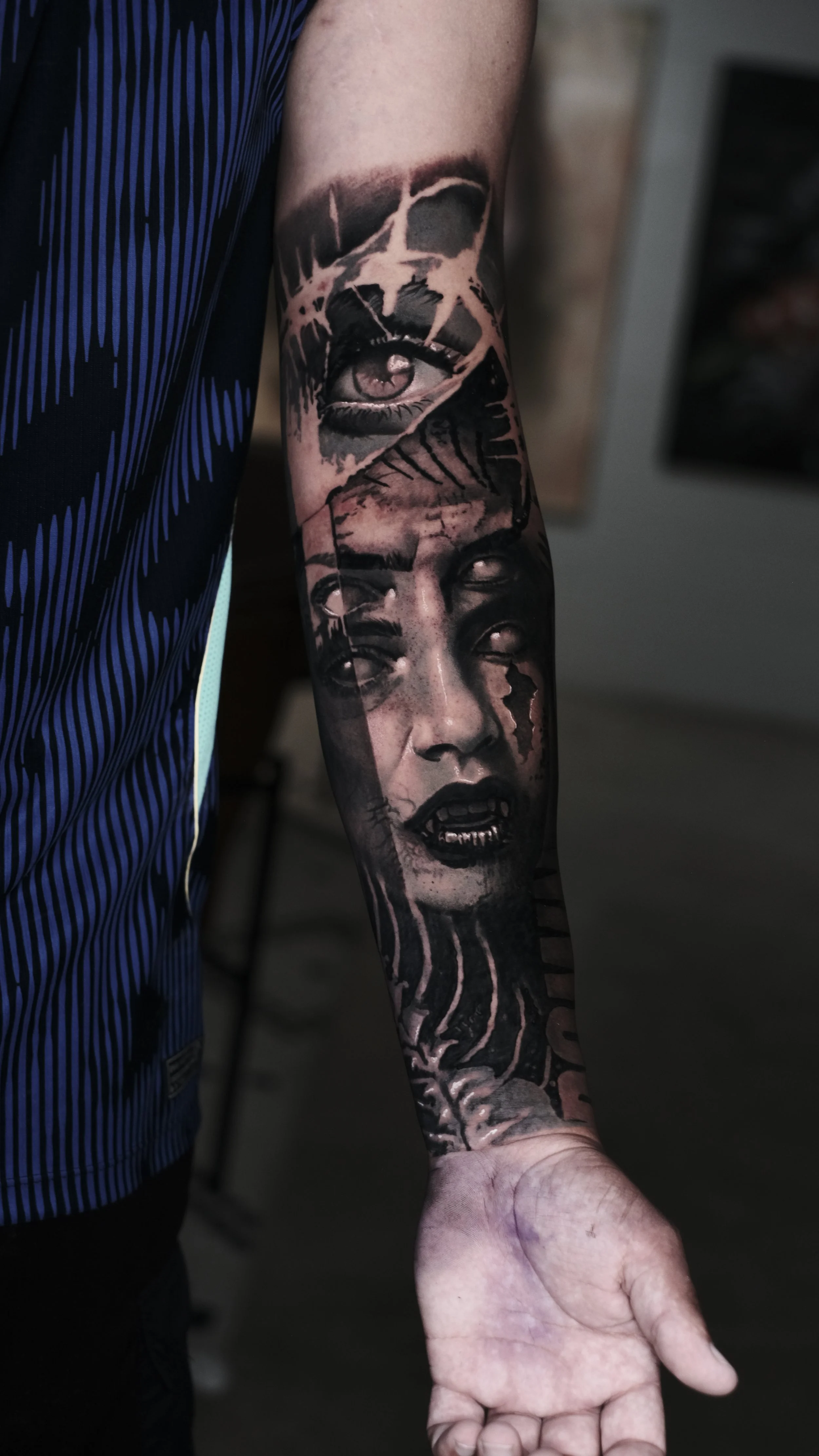 Tattoo of a woman's face with tears and a skull above her eye on a person's arm.