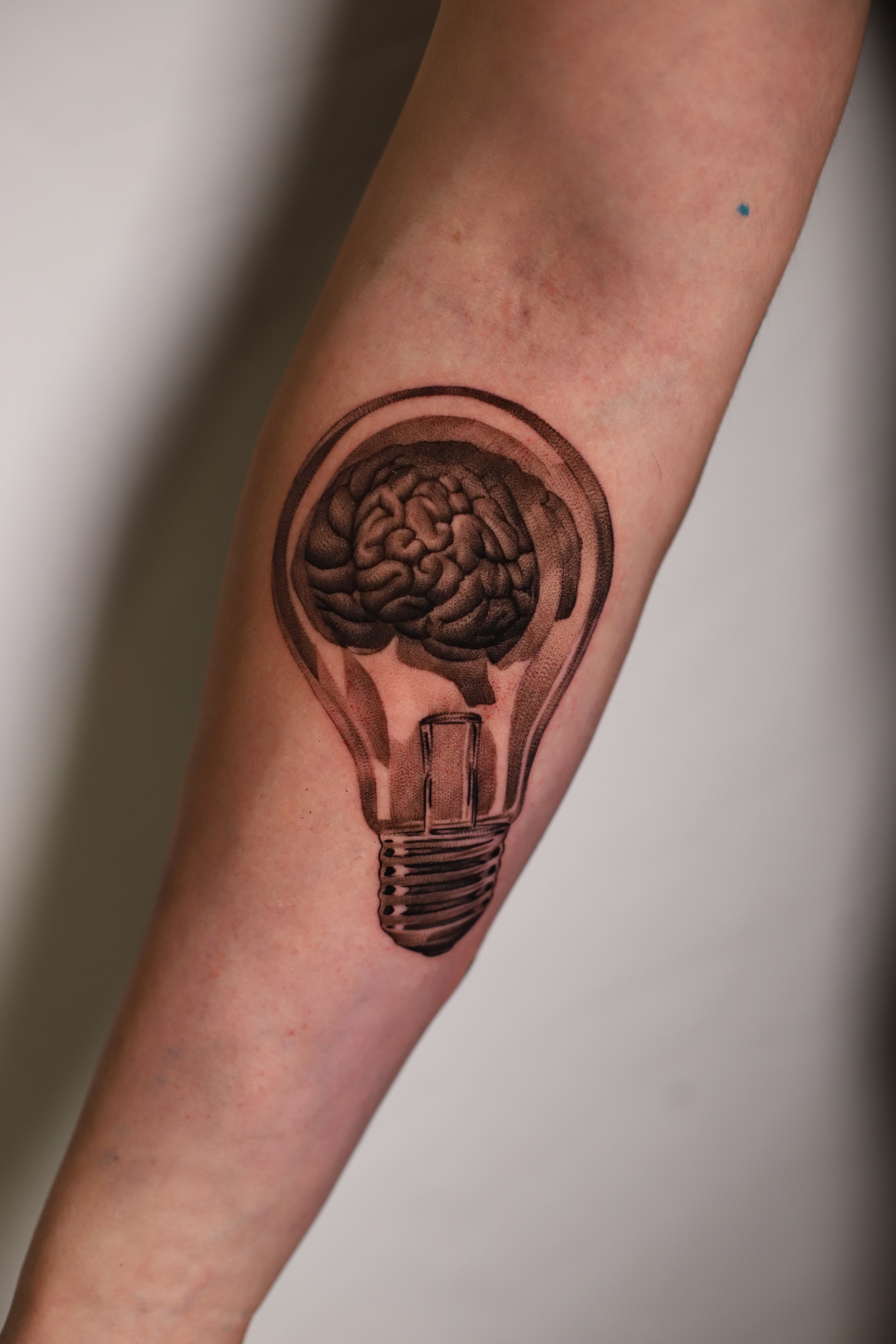Tattoo of a brain inside a lightbulb on a person's forearm.
