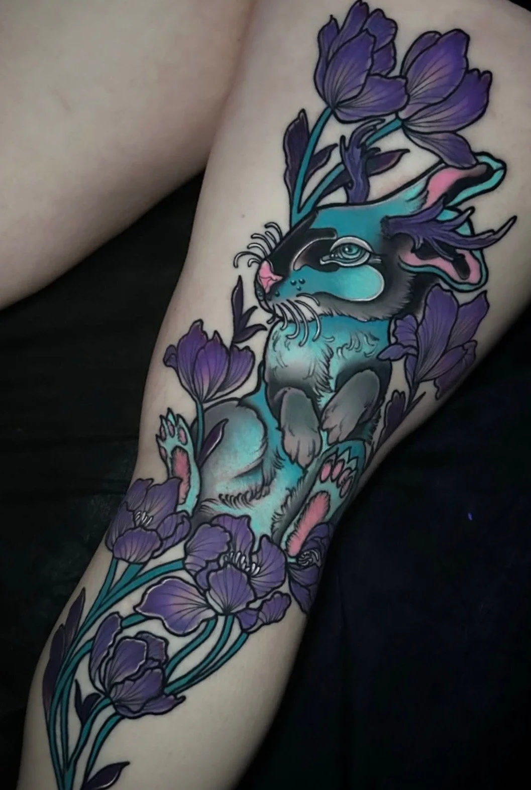 Colorful tattoo of a stylized animal, possibly a feline, intertwined with purple flowers and teal accents.